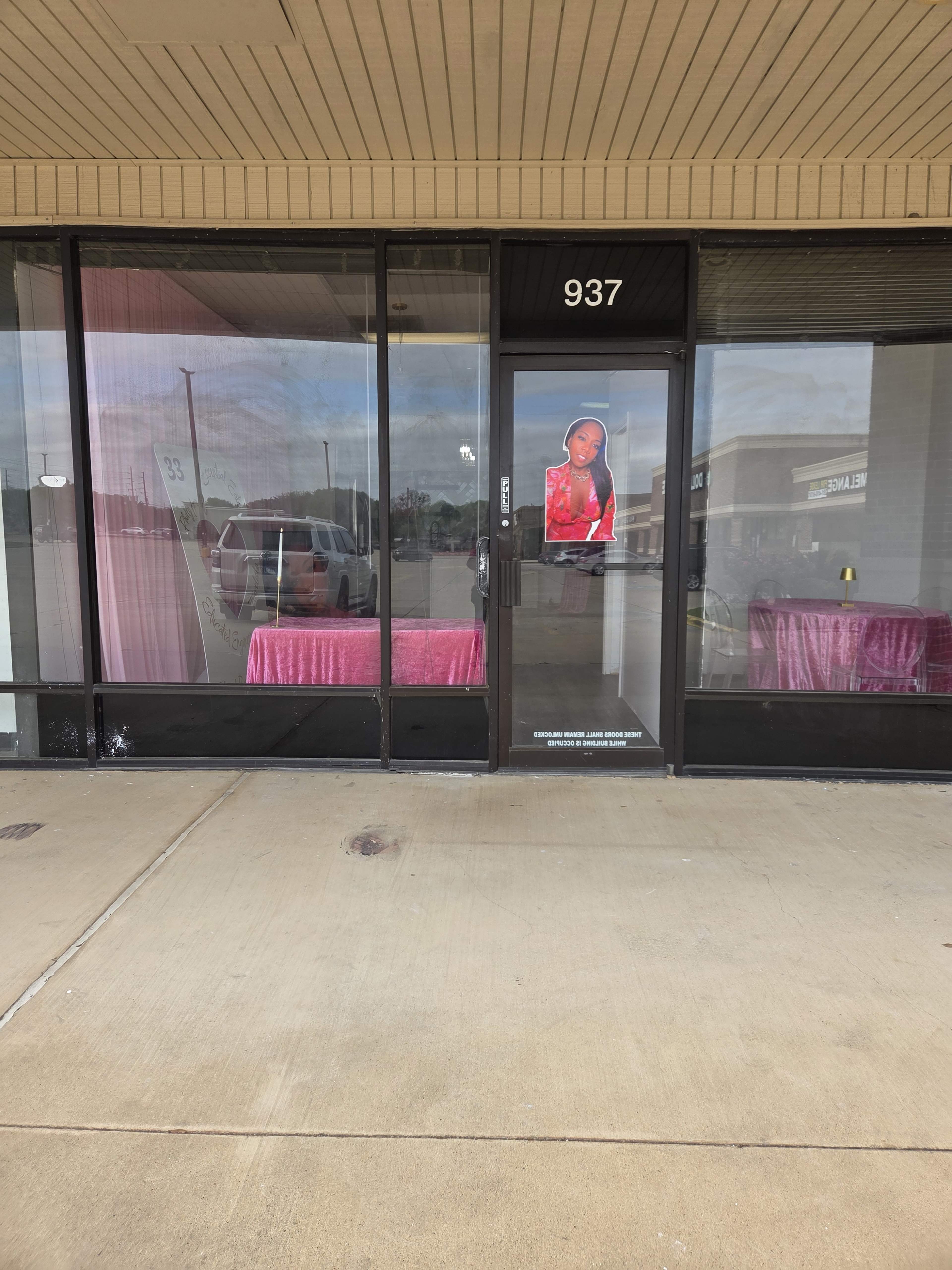 The image shows a storefront with large glass windows displaying pink fabric inside and a cutout figure of a woman in red on the door.