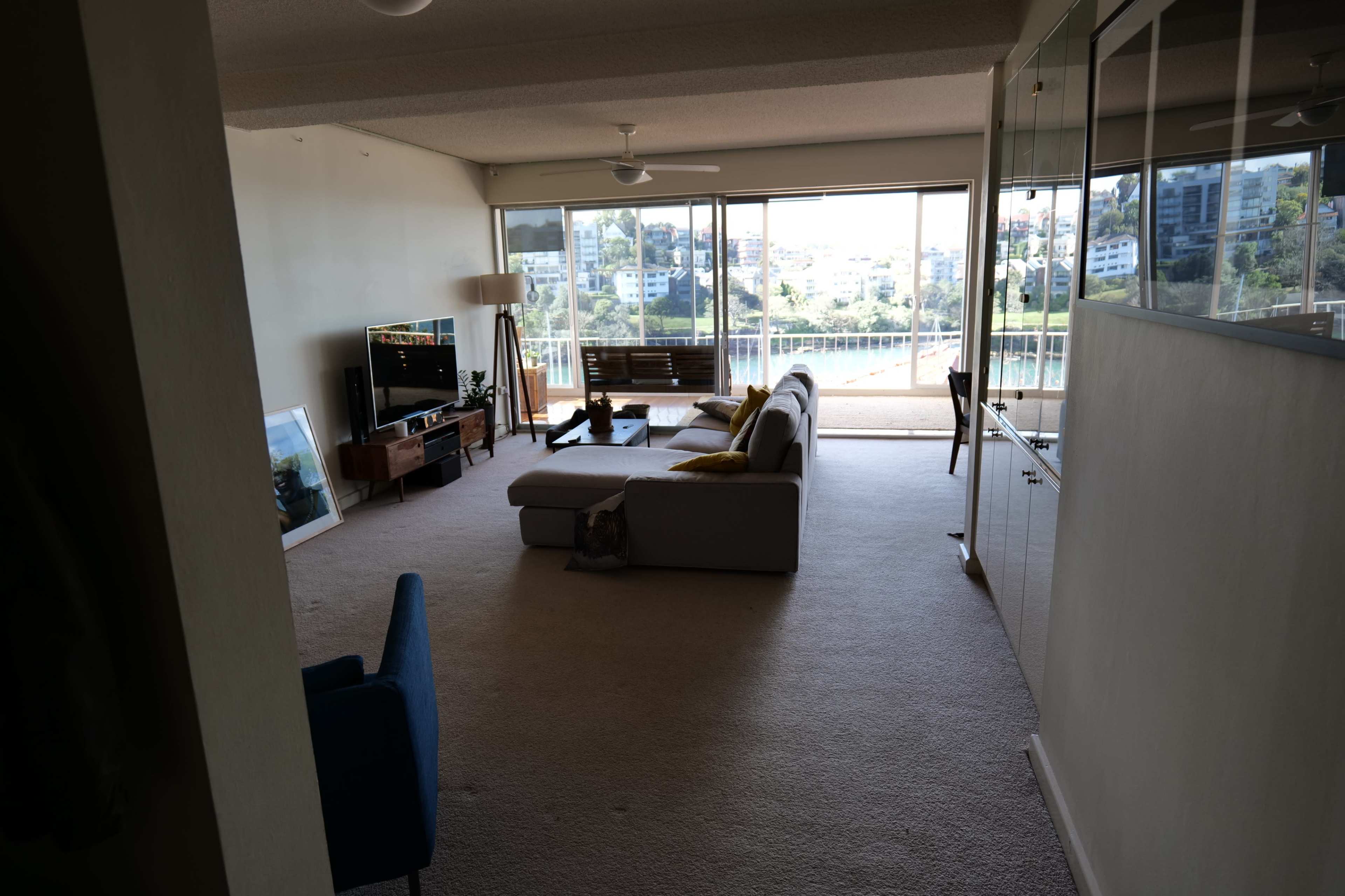 A spacious living room features a large window with a view of hills and houses, a sofa, a coffee table, and a TV unit.