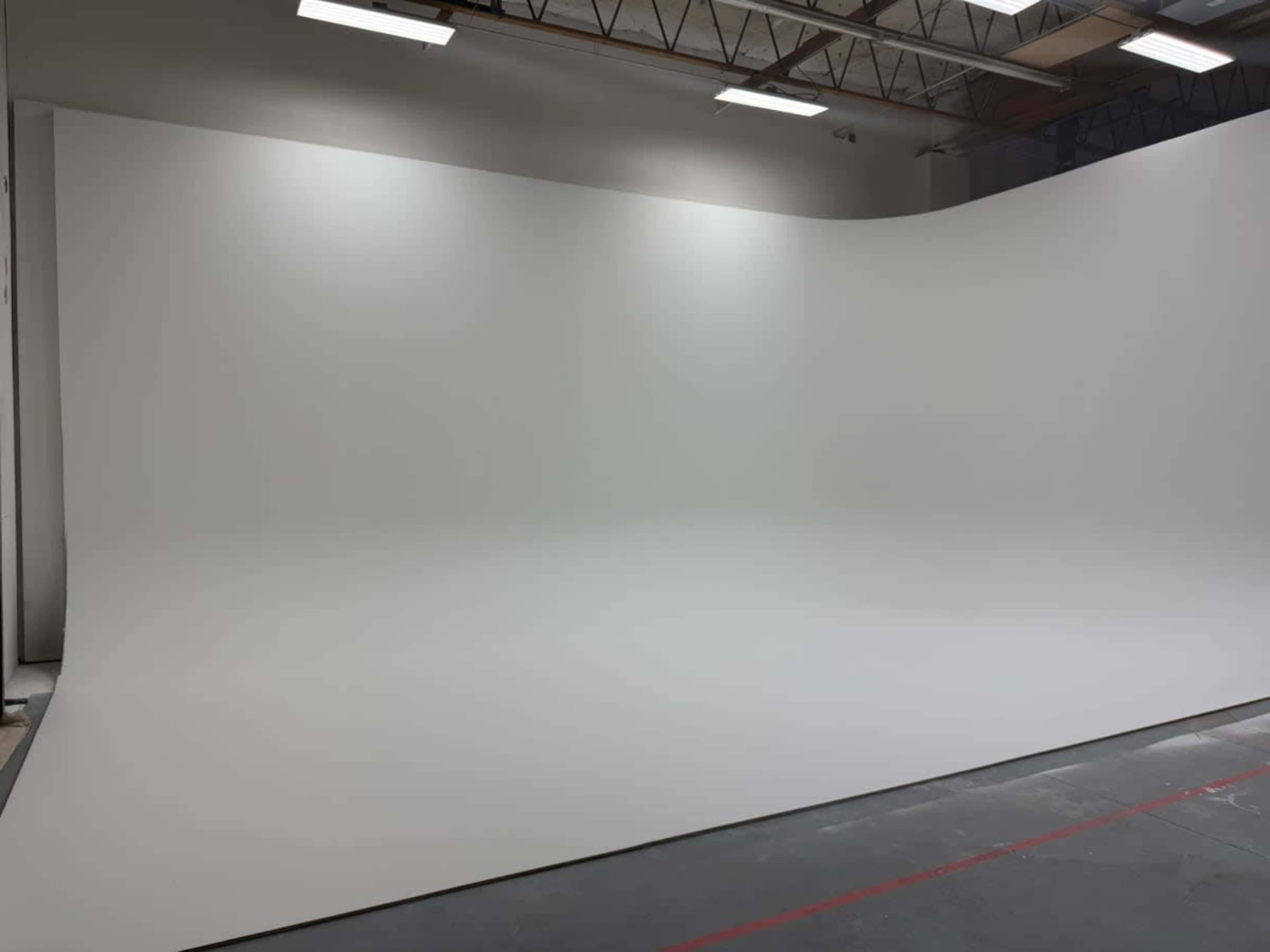 The image shows a spacious studio with a smooth, curved white backdrop and overhead lighting.