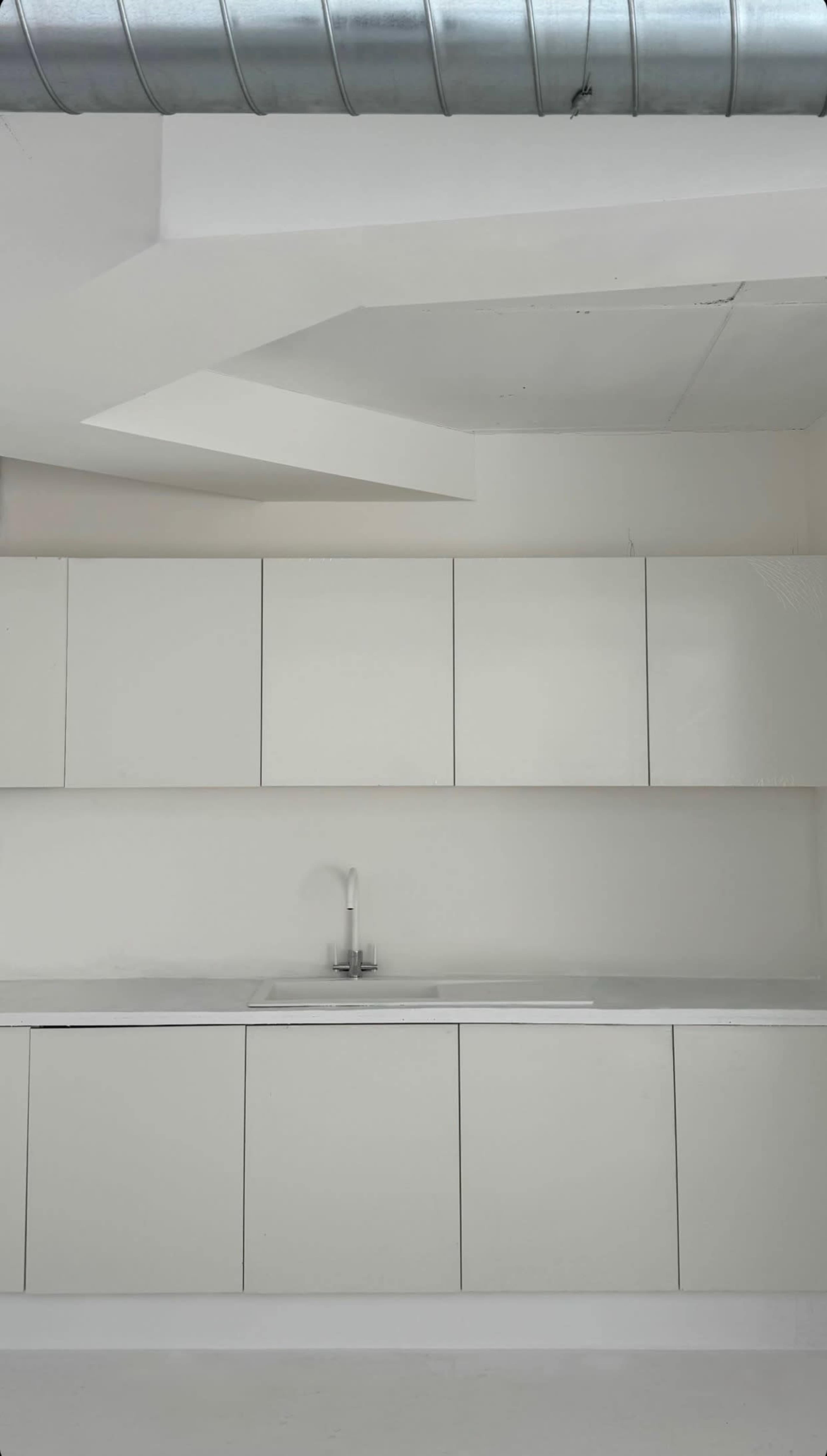 A minimalist kitchen with white cabinetry and a sink against a bright wall.