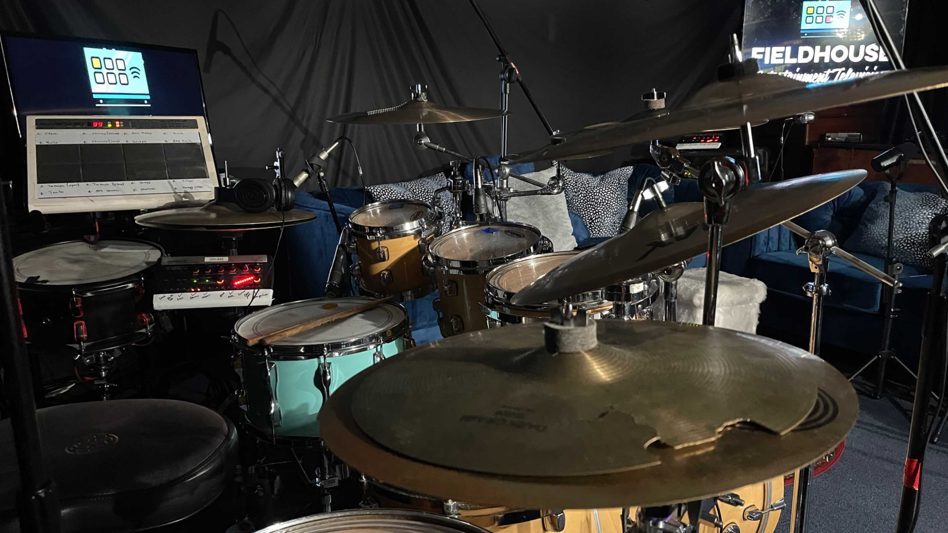 A drum set with various instruments, microphones, and a computer setup in a music studio.