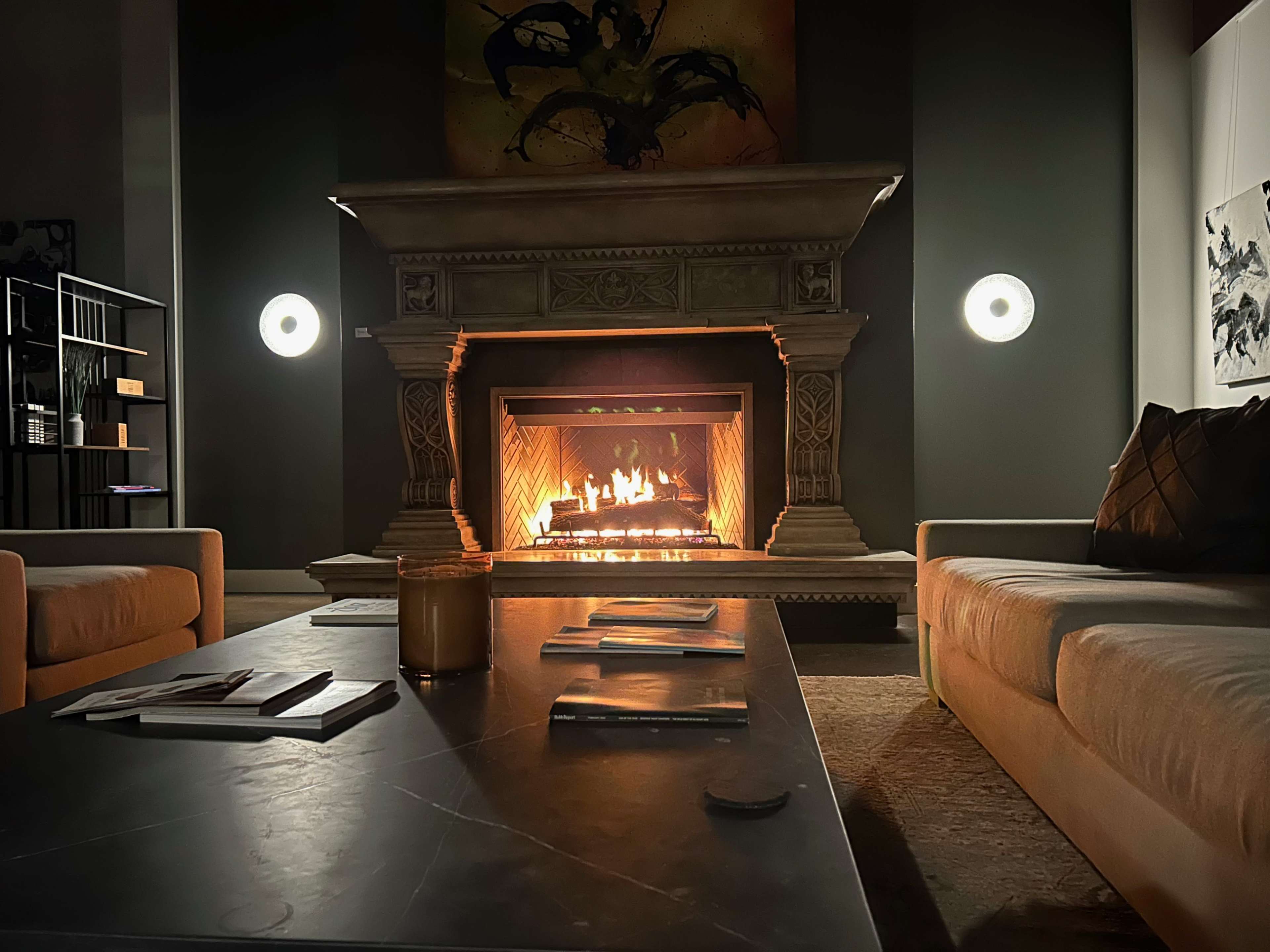 A cozy living room features a stone fireplace with a roaring fire, surrounded by soft sofas and a low coffee table.