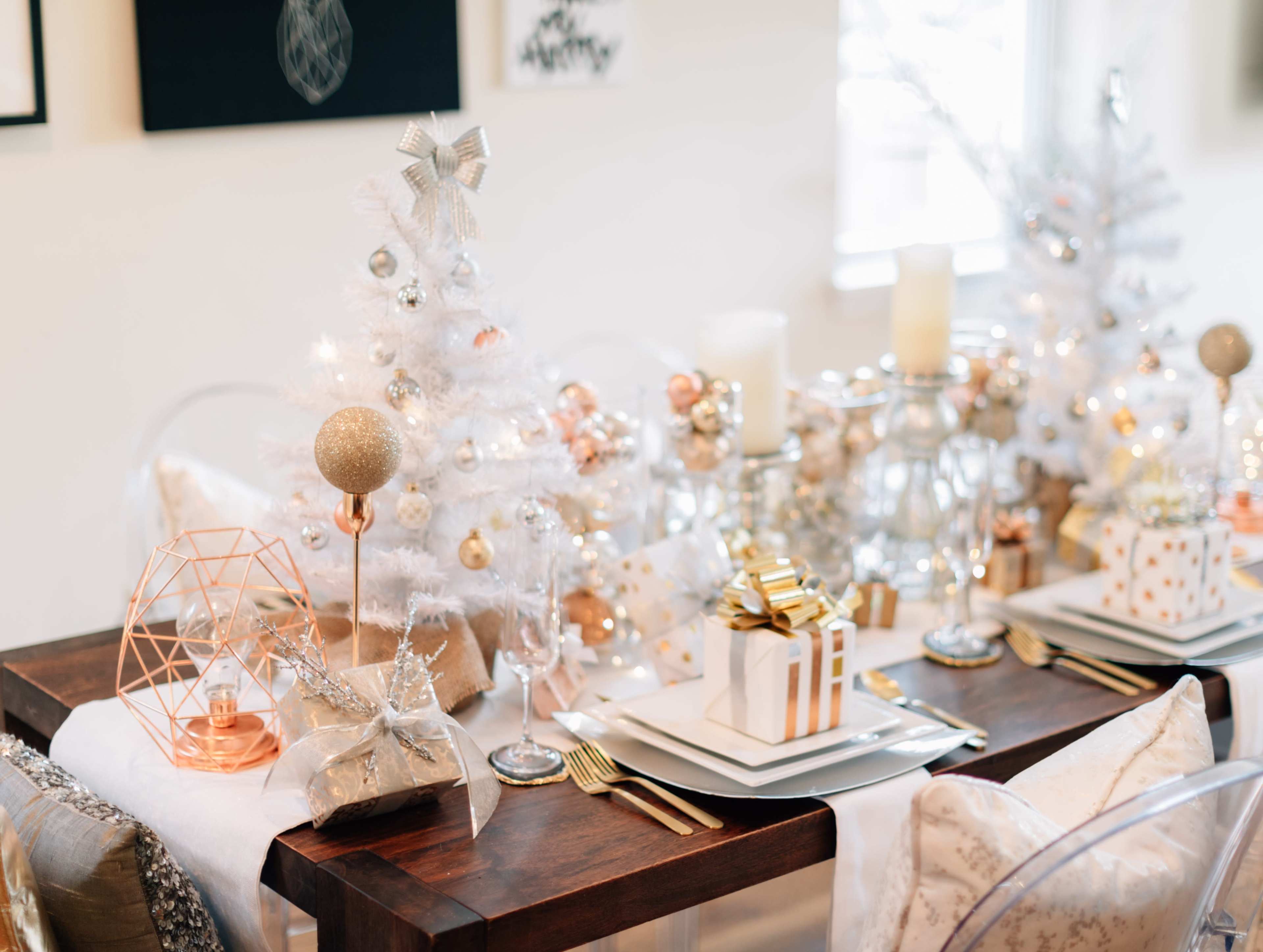 A holiday dining table is elegantly set with a small white Christmas tree, decorative candles, and gift boxes.