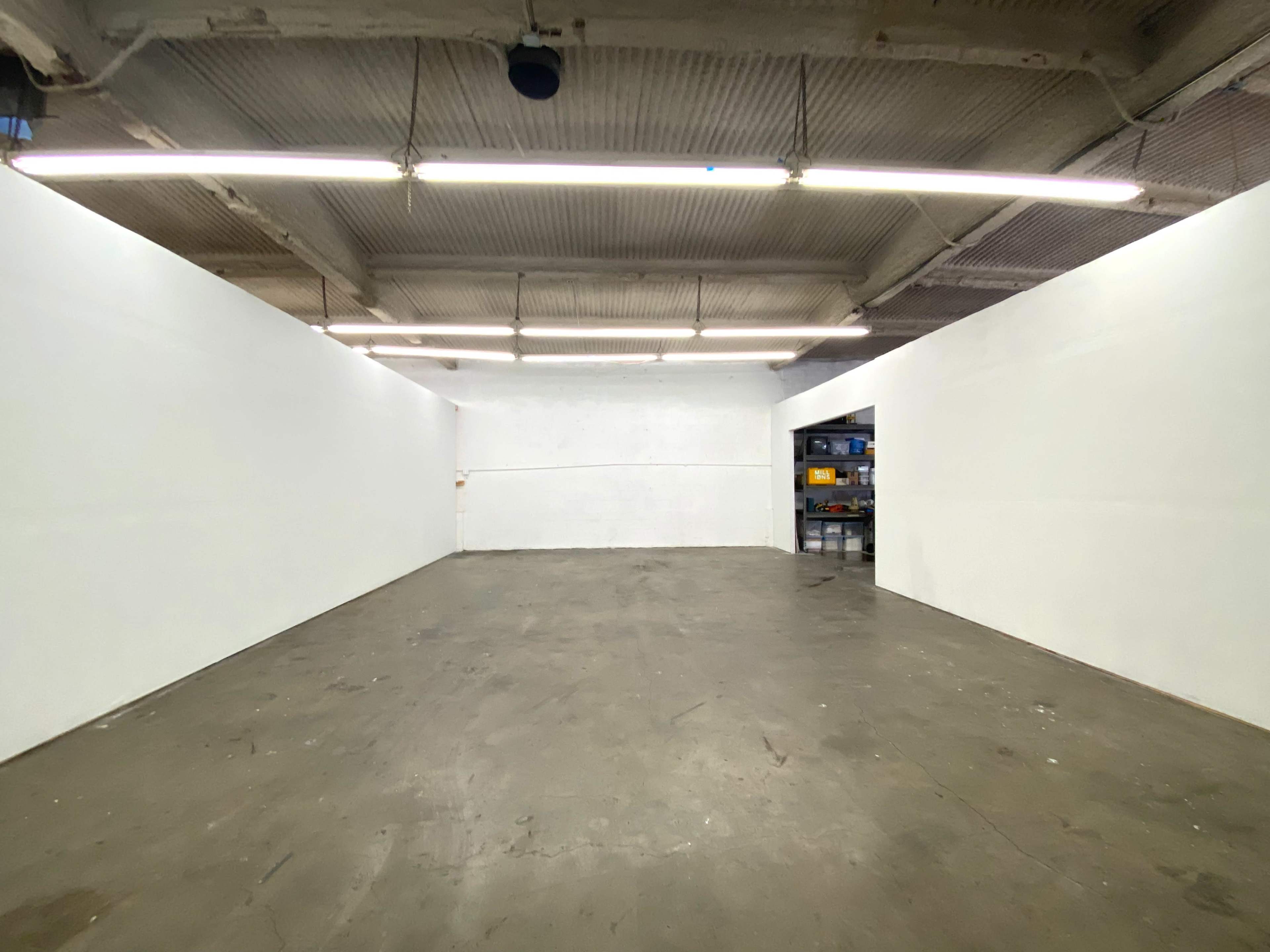 An empty, white-walled room with a concrete floor and overhead lighting.