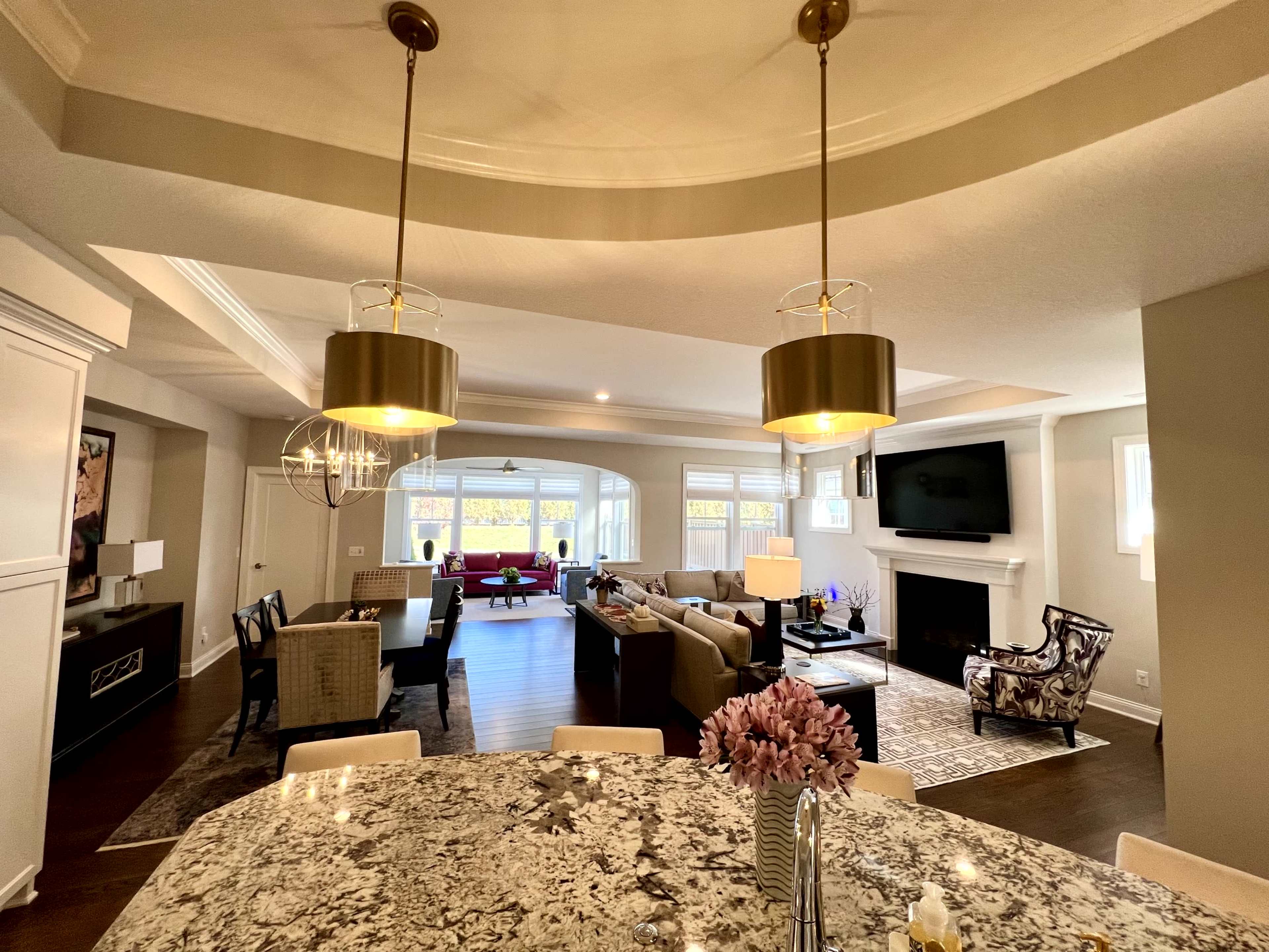 The image shows an open-concept living space featuring a kitchen with a granite counter, dining area, and a comfortable living room with large windows and a fireplace.