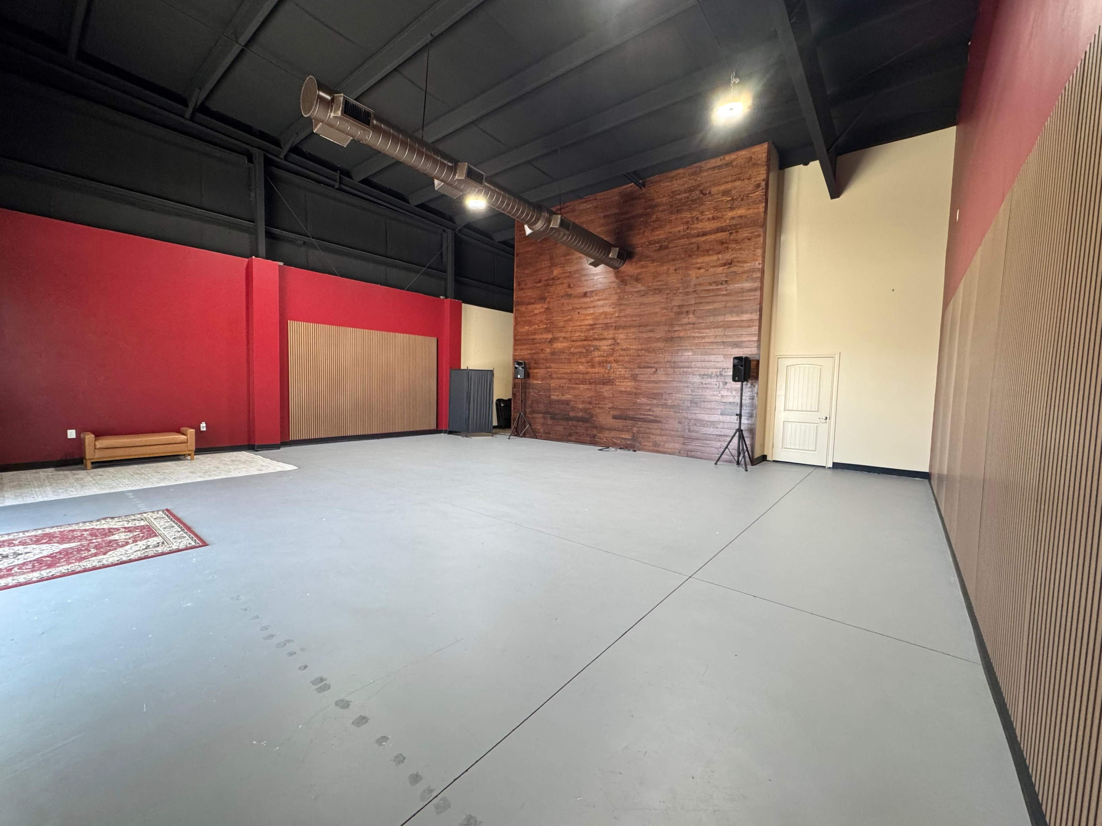 The image shows a spacious interior with a wooden accent wall, a red painted section, and an area rug on the floor.