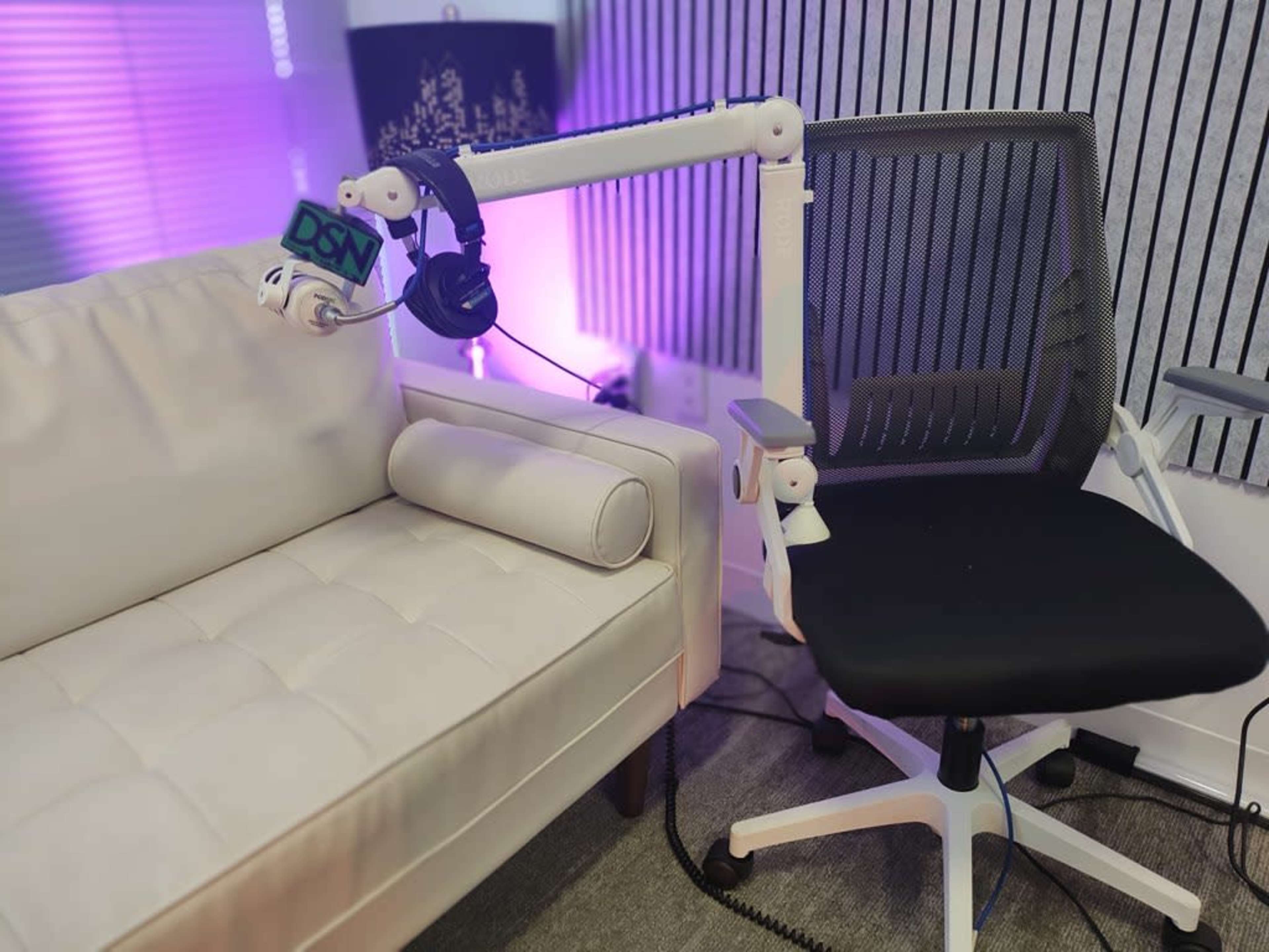 The image shows a white couch next to a black ergonomic office chair, both positioned in a room with purple lighting.