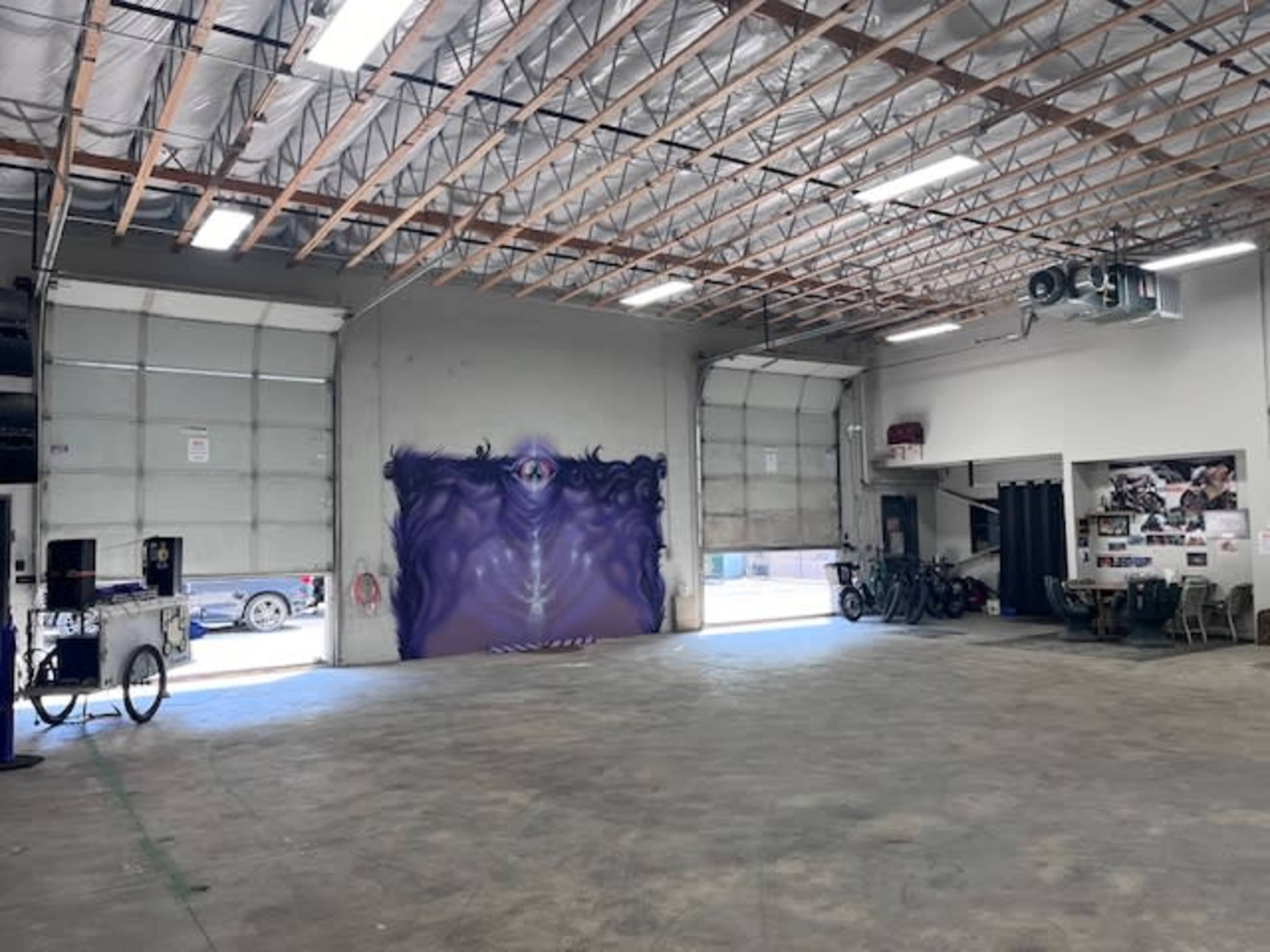 A spacious garage with a purple mural on the far wall and two large bay doors open to the outside.