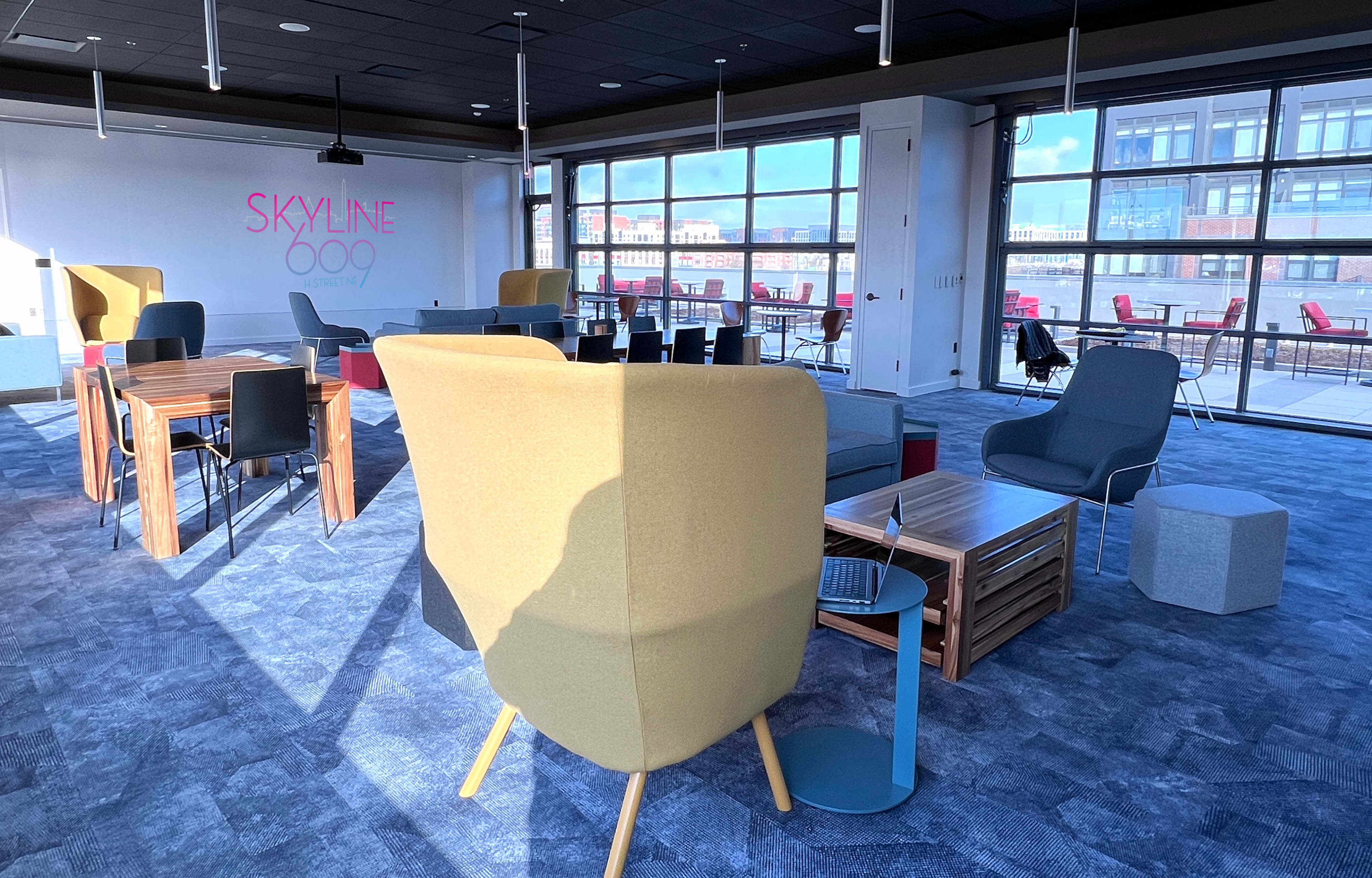 A modern open workspace with various seating arrangements, desks, and large windows offering a view of the skyline.