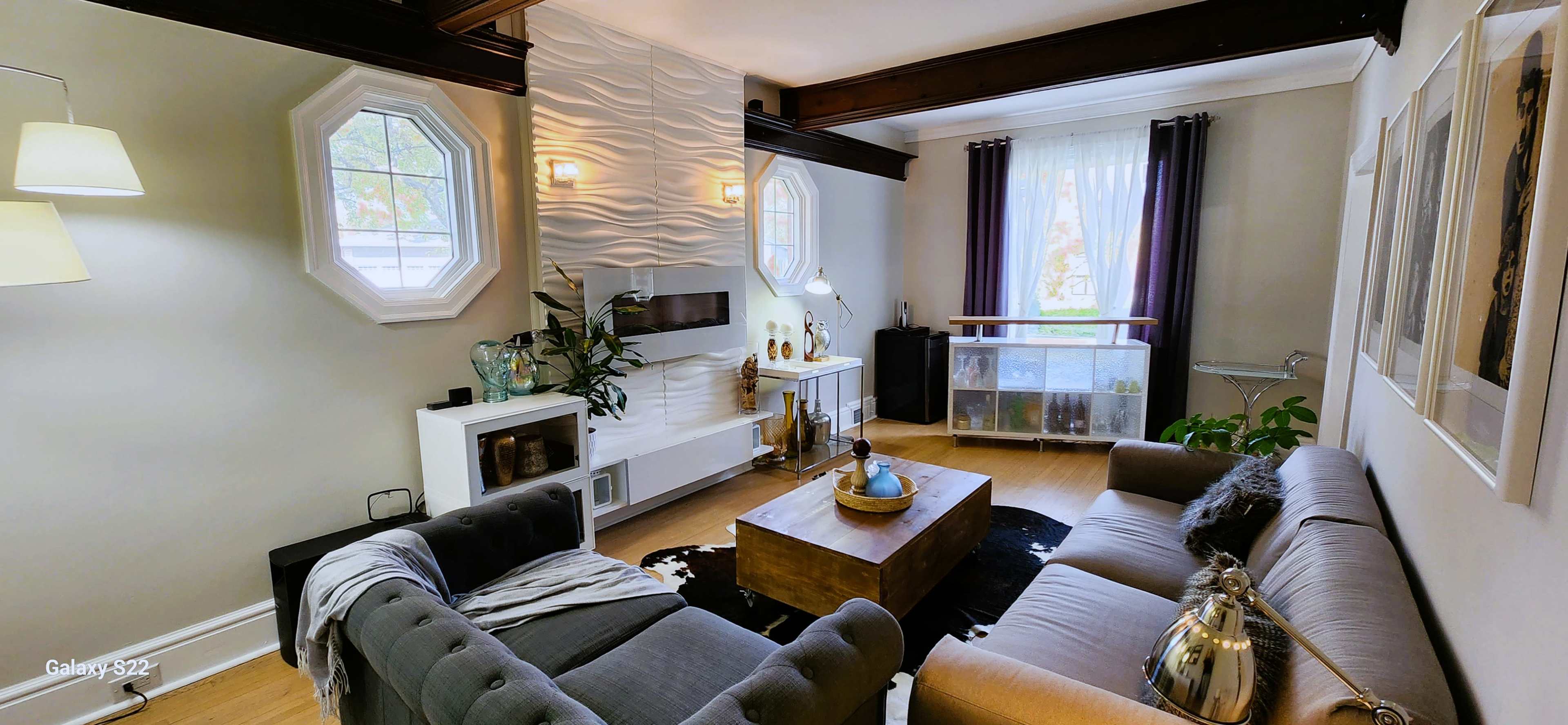 A living room featuring a sectional sofa, a wooden coffee table, a modern entertainment unit, and large windows with light curtains.