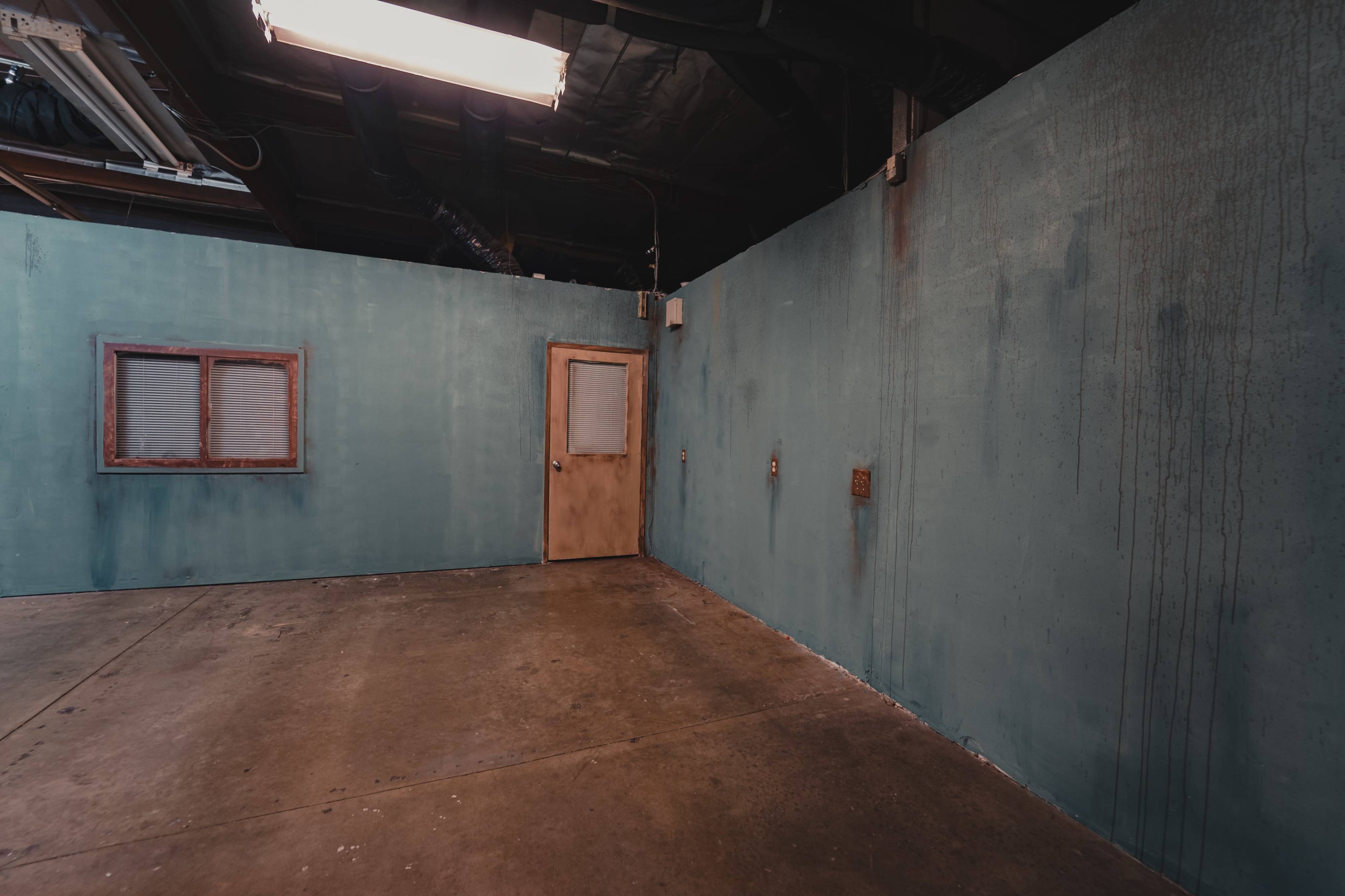 An empty room with teal walls, a concrete floor, a small window, and a door.