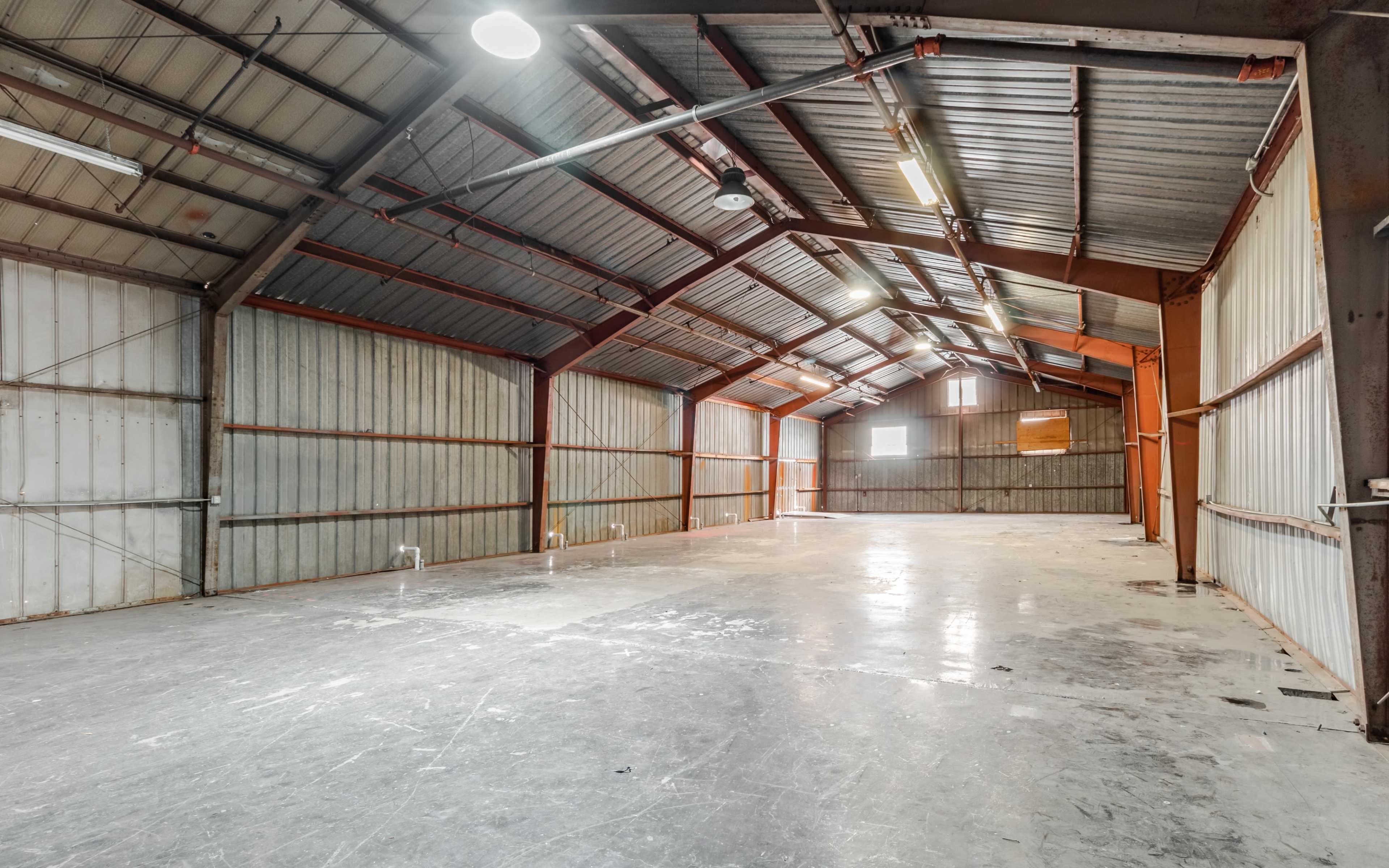 A large, empty industrial storage space with a high metal roof and concrete floor.