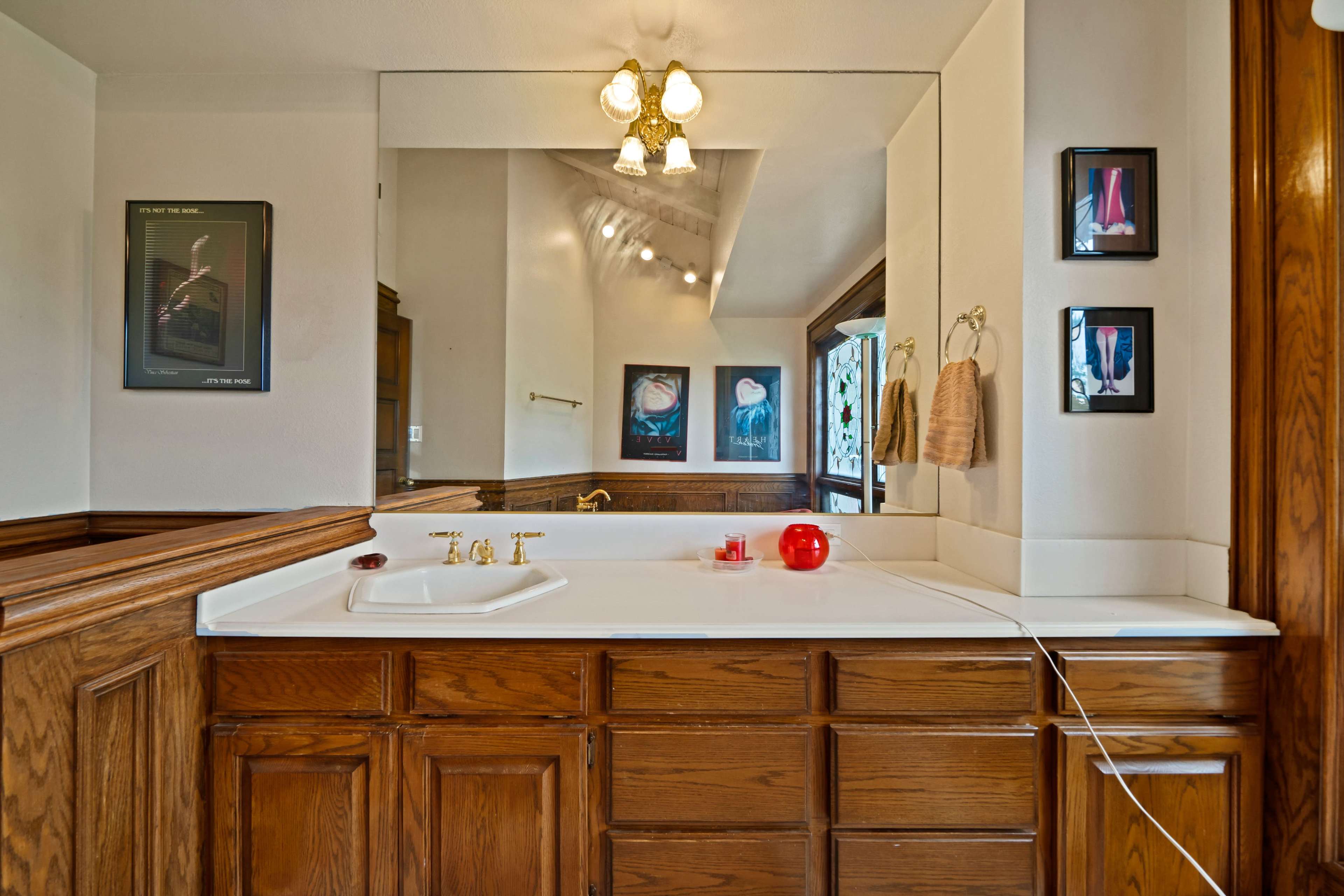 The image shows a bathroom with a wooden vanity, a sink, and a large mirror, illuminated by three light fixtures above.