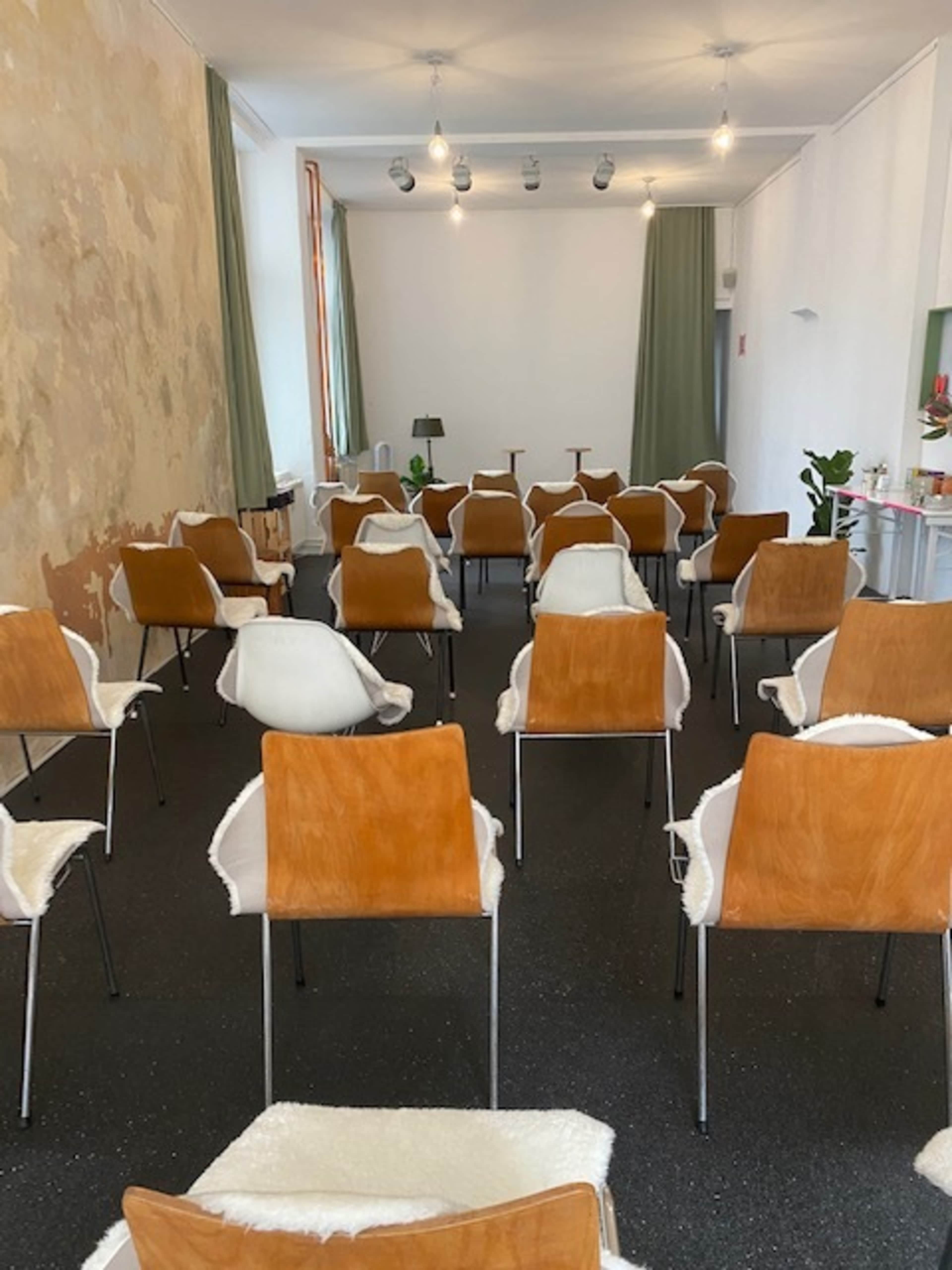 A room arranged with rows of wooden chairs featuring white seat covers, facing a blank wall and illuminated by overhead lights.