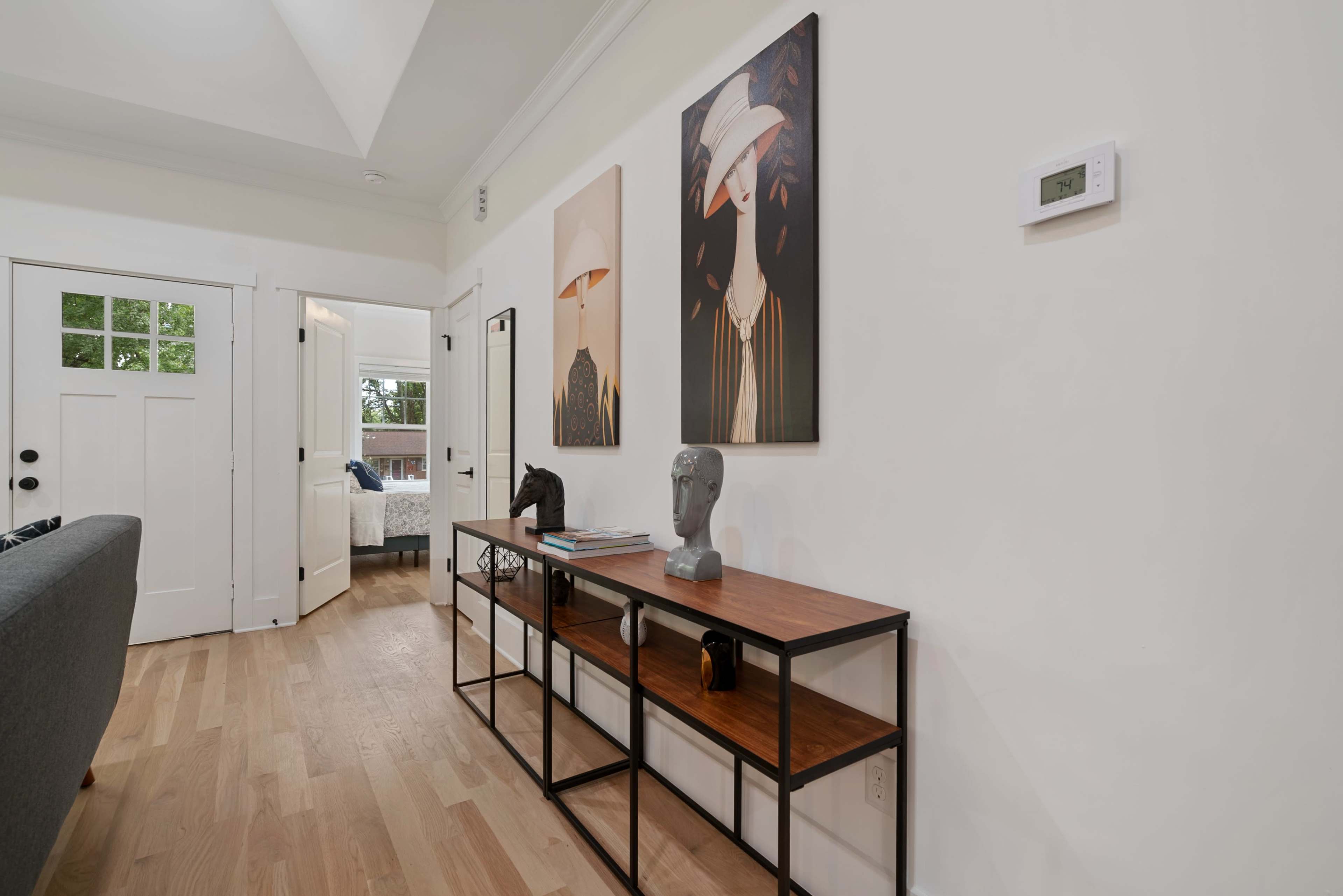 A narrow console table with artwork above it against a white wall, with a door leading to another room partially open in the background.