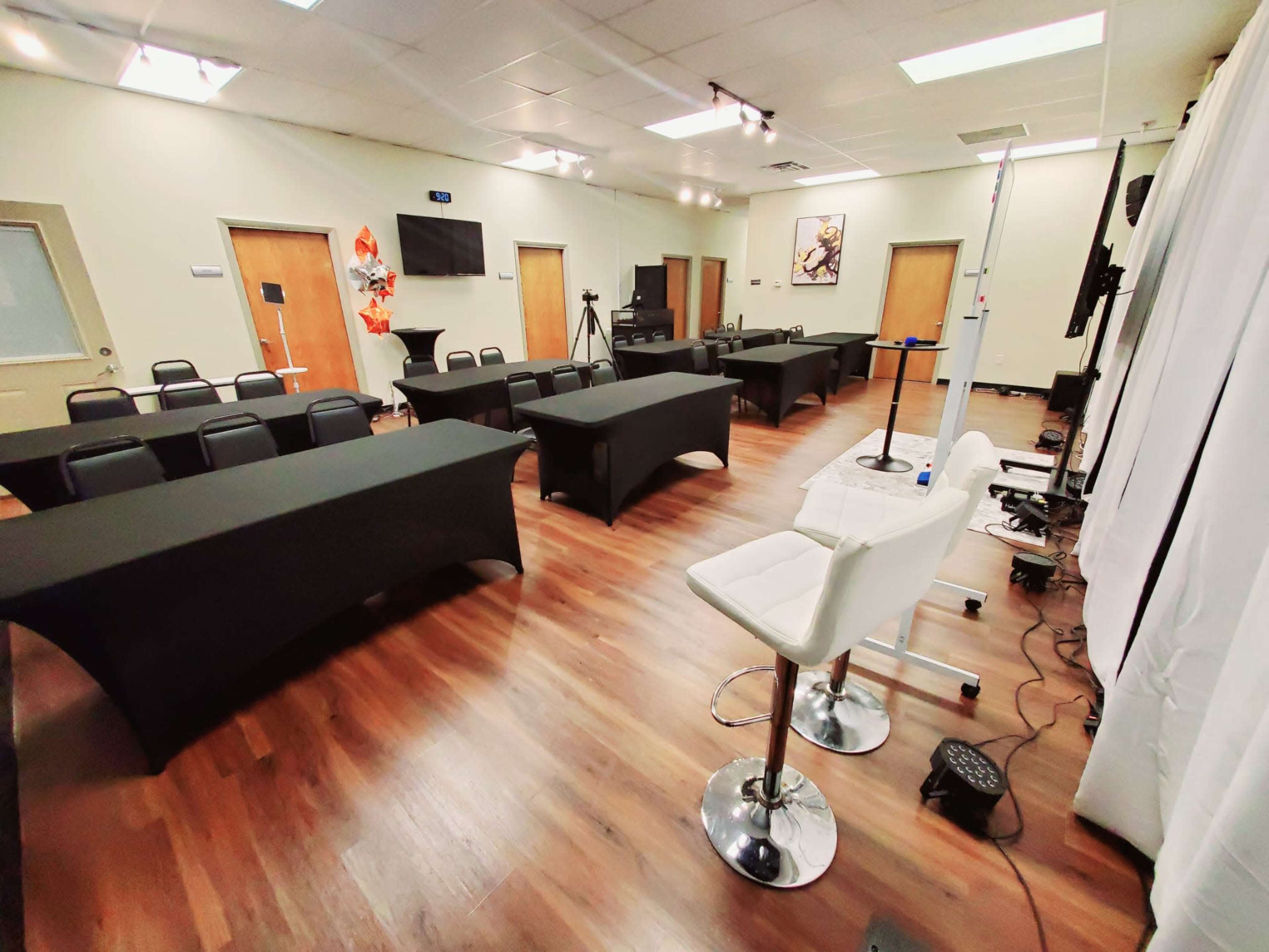 A conference room set up with several tables covered in black cloth, arranged in a U-shape, and equipped with chairs and filming equipment.