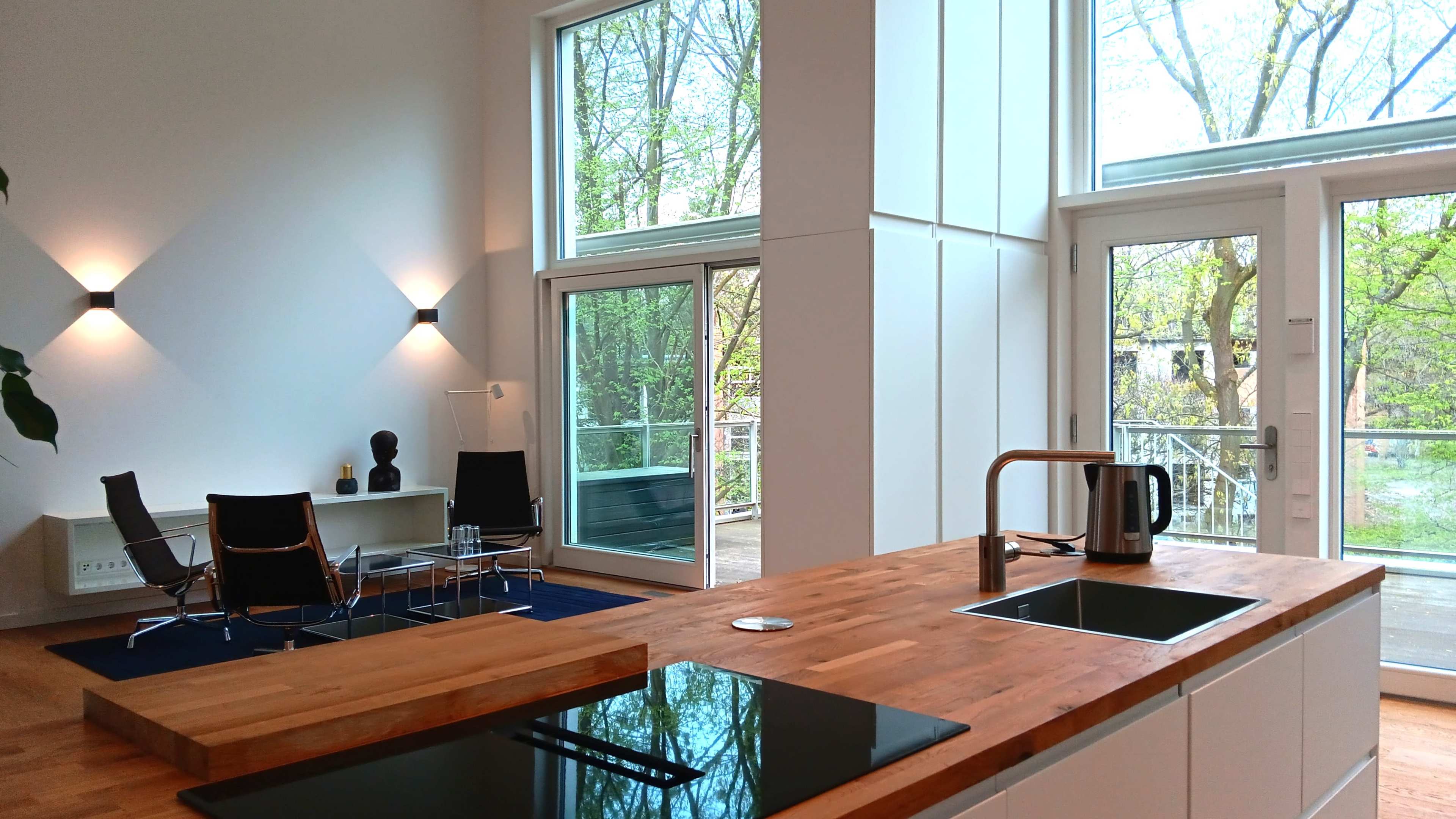 A modern kitchen and living area with large windows, a wooden countertop, and minimalist furniture.