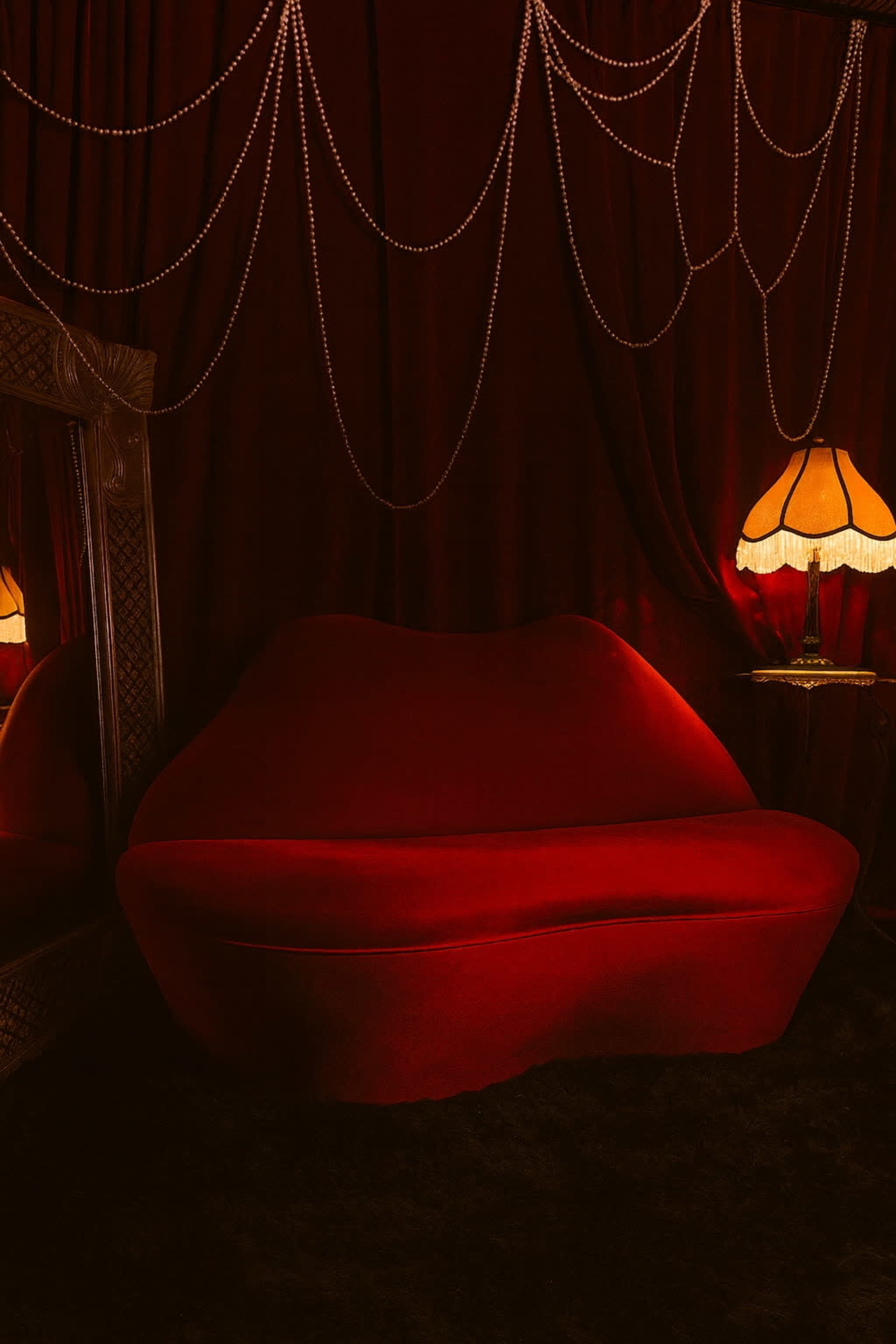 The image features a red velvet sofa positioned against a dark curtain backdrop, with a decorative mirror and a vintage lamp illuminating the scene.