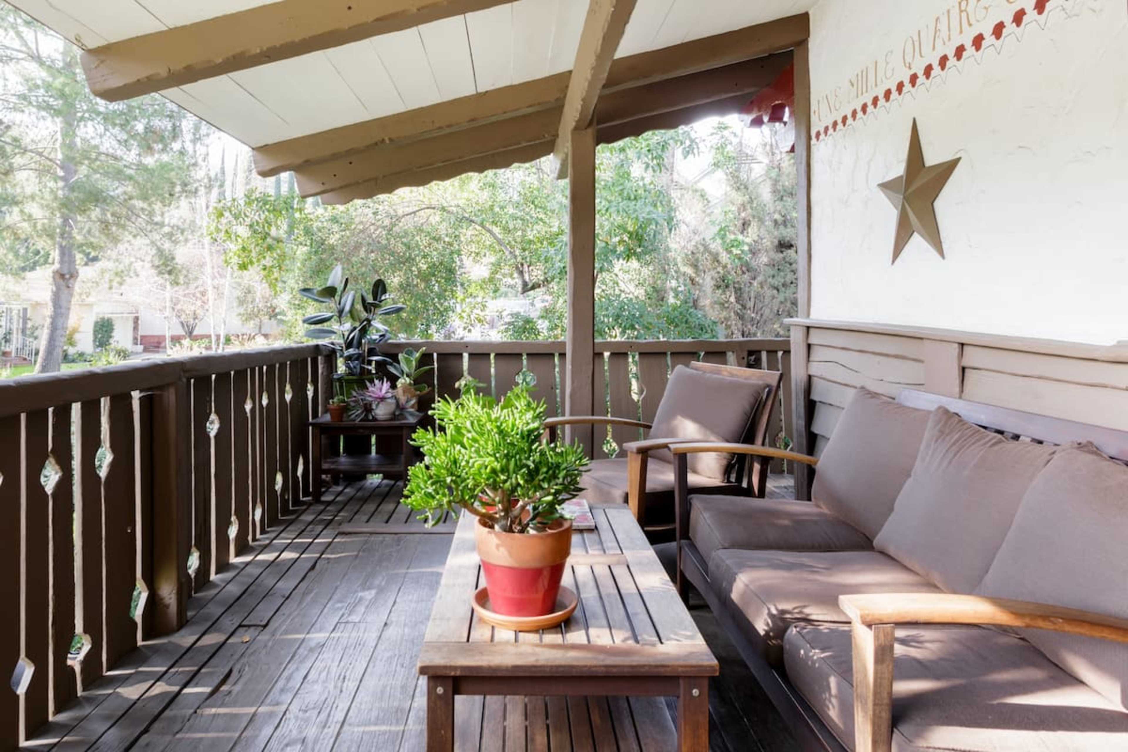 A wooden porch features brown furniture, a potted plant, and a decorative wall with a star and text.