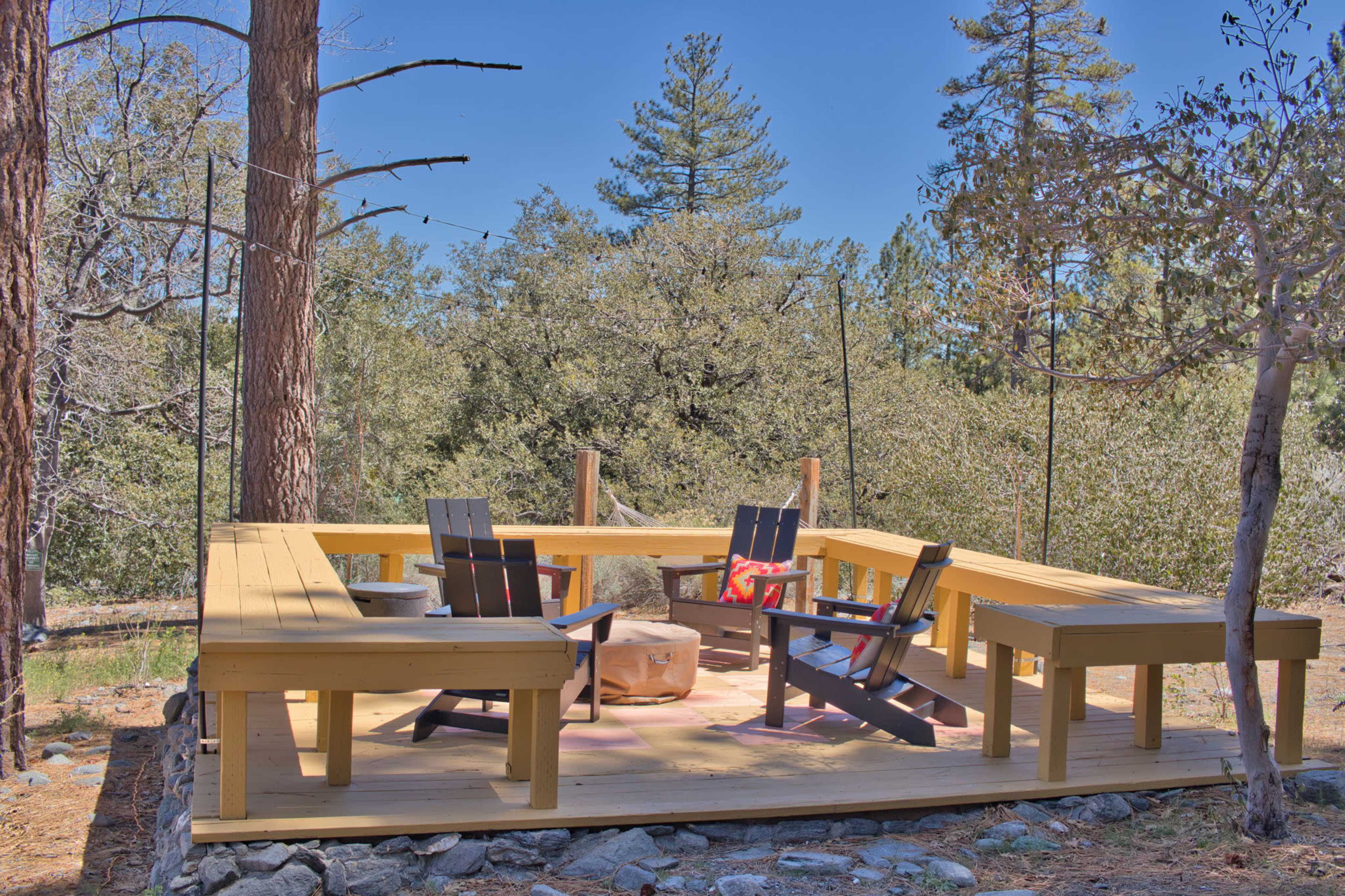 A wooden deck with seating is set in a forested area, surrounded by trees and natural landscape.