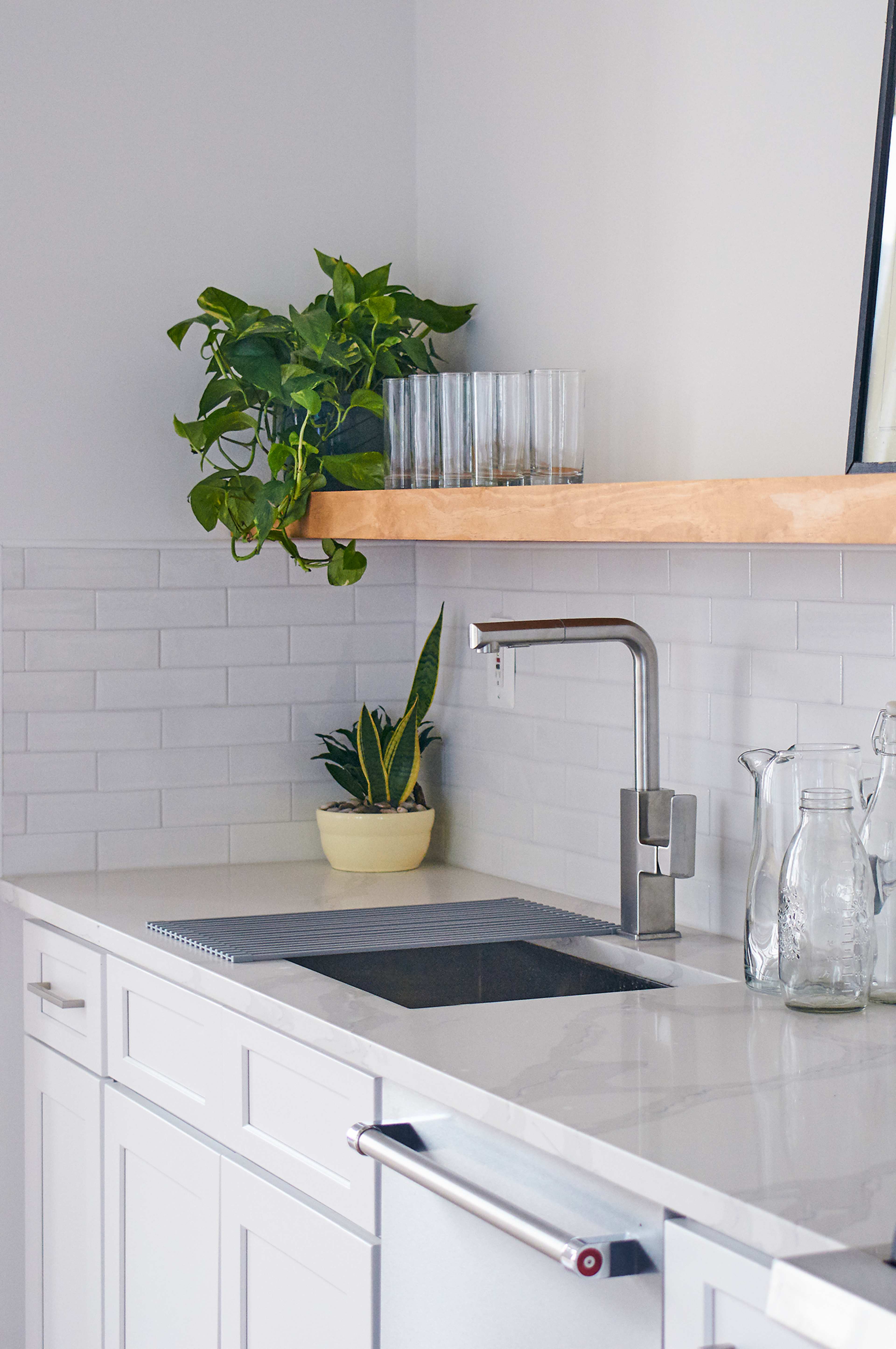 A modern kitchen with white cabinetry, a sink with a sleek faucet, and a shelf holding glasses and plants above the countertop.