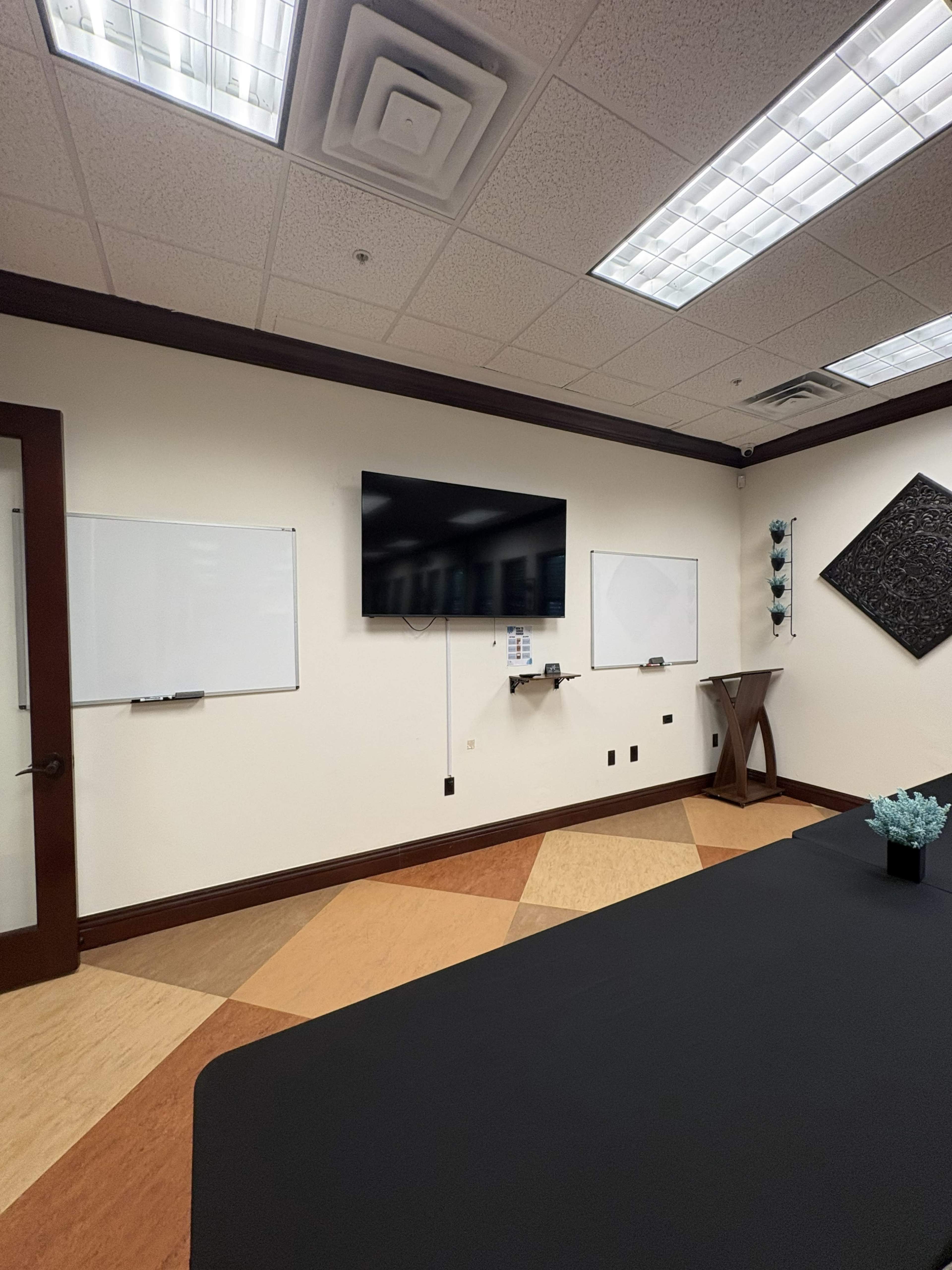 The image shows a modern conference room featuring a large television on the wall, two whiteboards, and a dark tablecloth covering a long table.