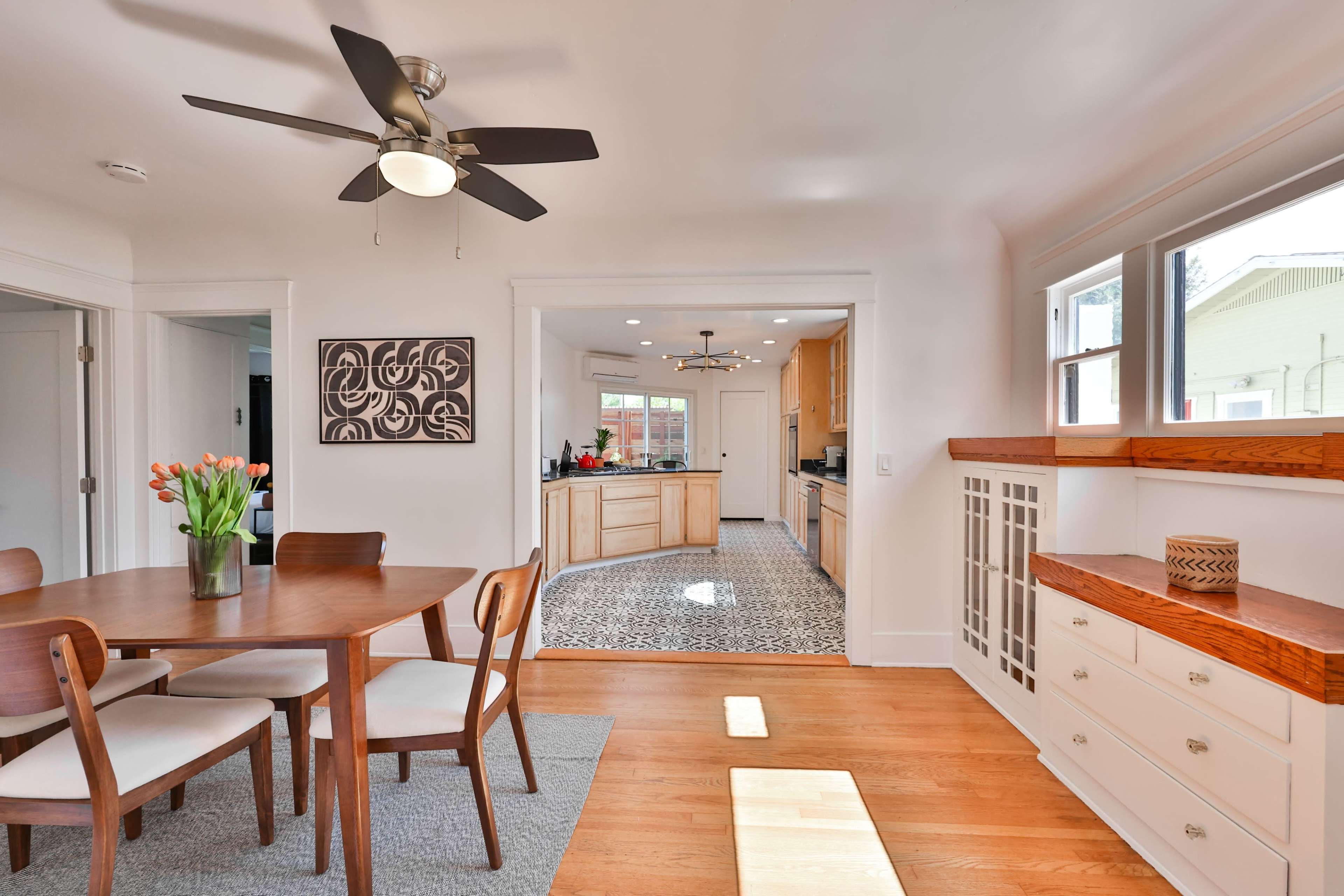A dining area with a circular table and chairs leads into a kitchen with wooden cabinetry and a patterned floor.