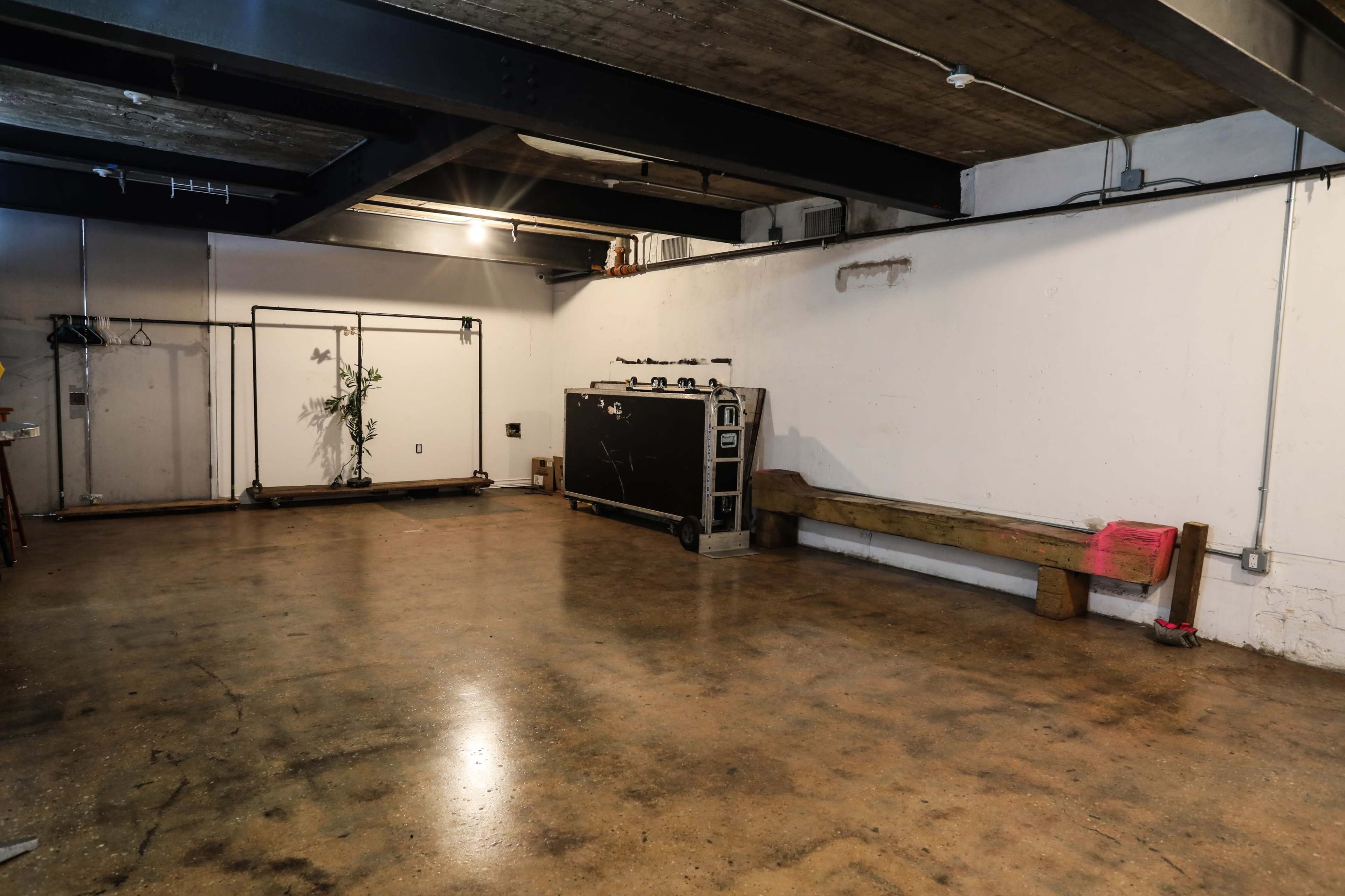 A spacious, empty room with a concrete floor and a few items along the walls, including a plant and a large case.
