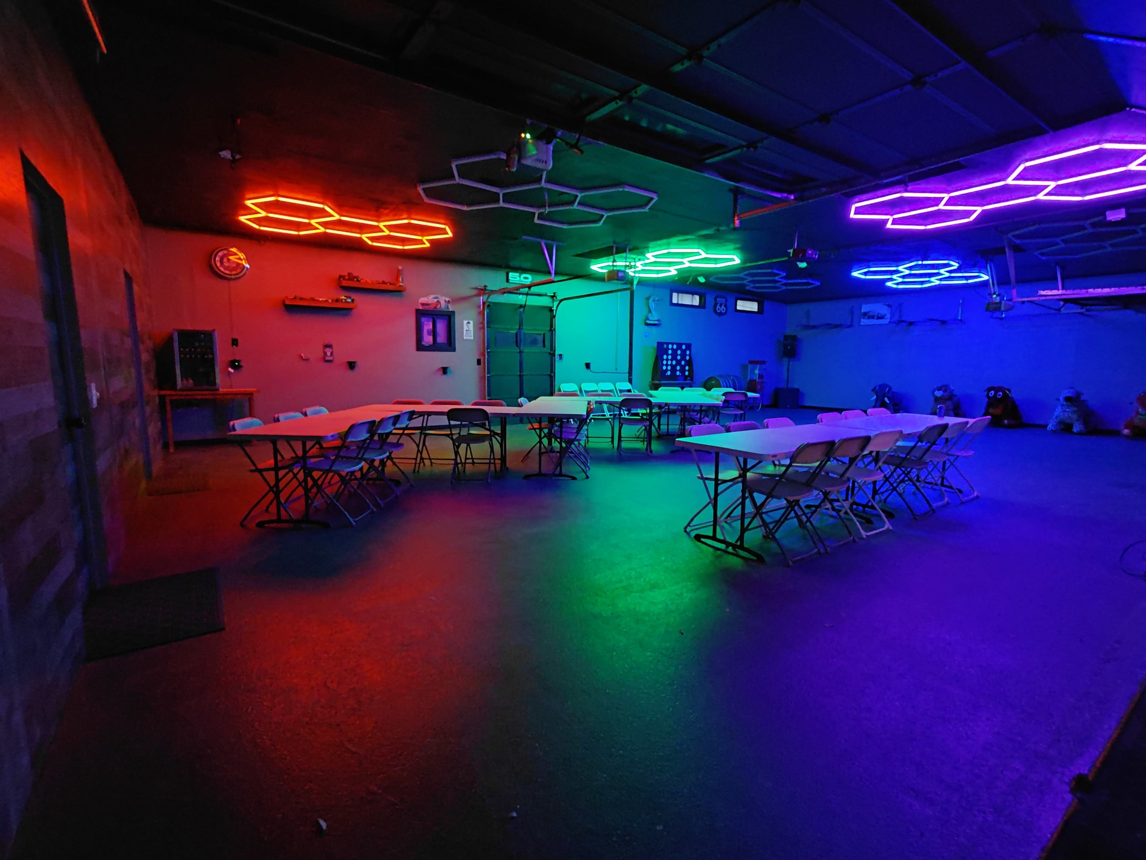 A spacious room is lit with colorful neon lights and arranged with tables and chairs set up in a circular layout.