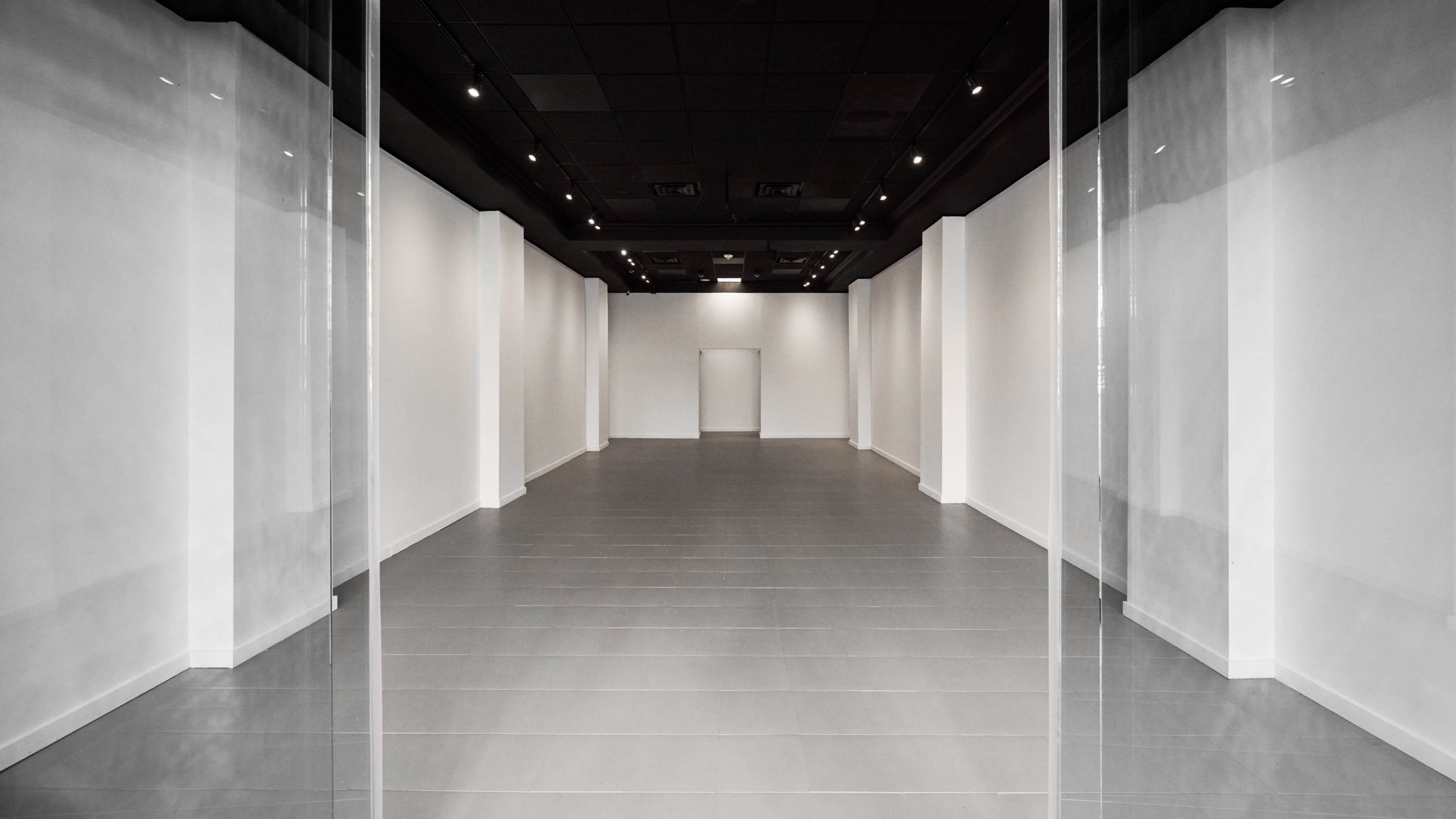 The image shows a spacious, empty interior with white walls and a polished floor, featuring a central door at the far end.
