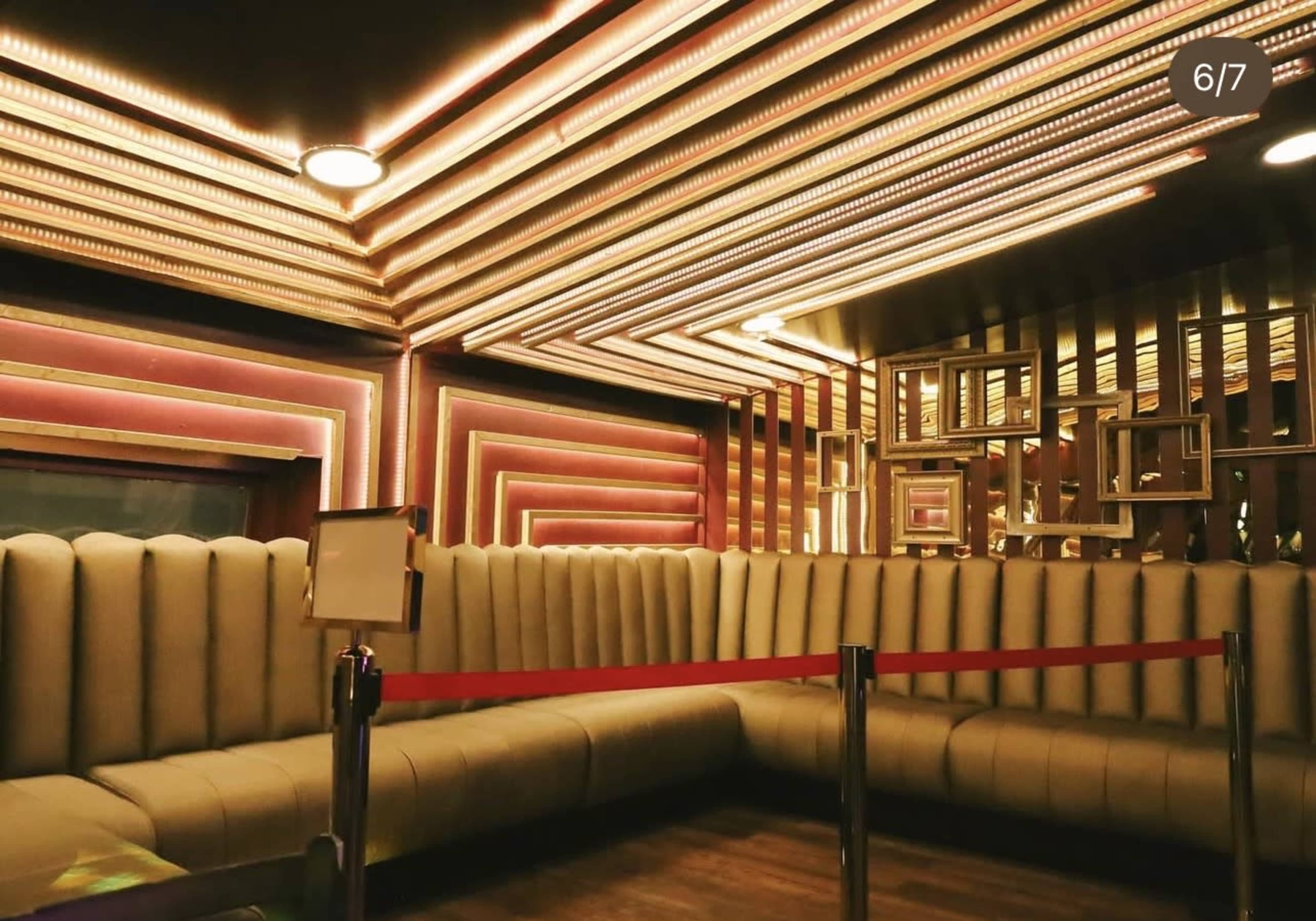 The image shows a modern lounge with a stylish seating area featuring soft, upholstered benches and ambient lighting along the ceiling.