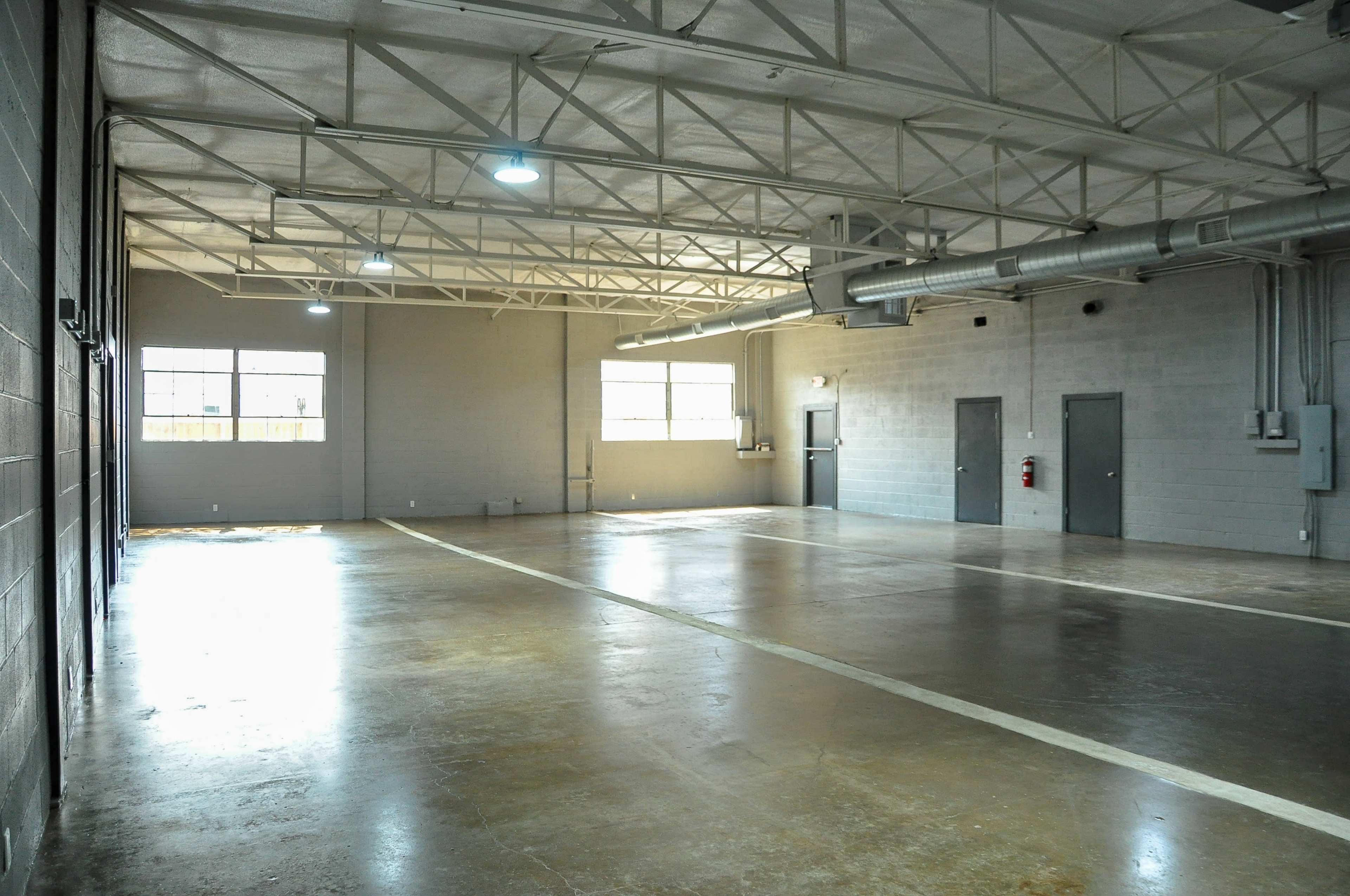 A large, empty industrial space with concrete flooring, several windows, and a high ceiling supported by steel beams.