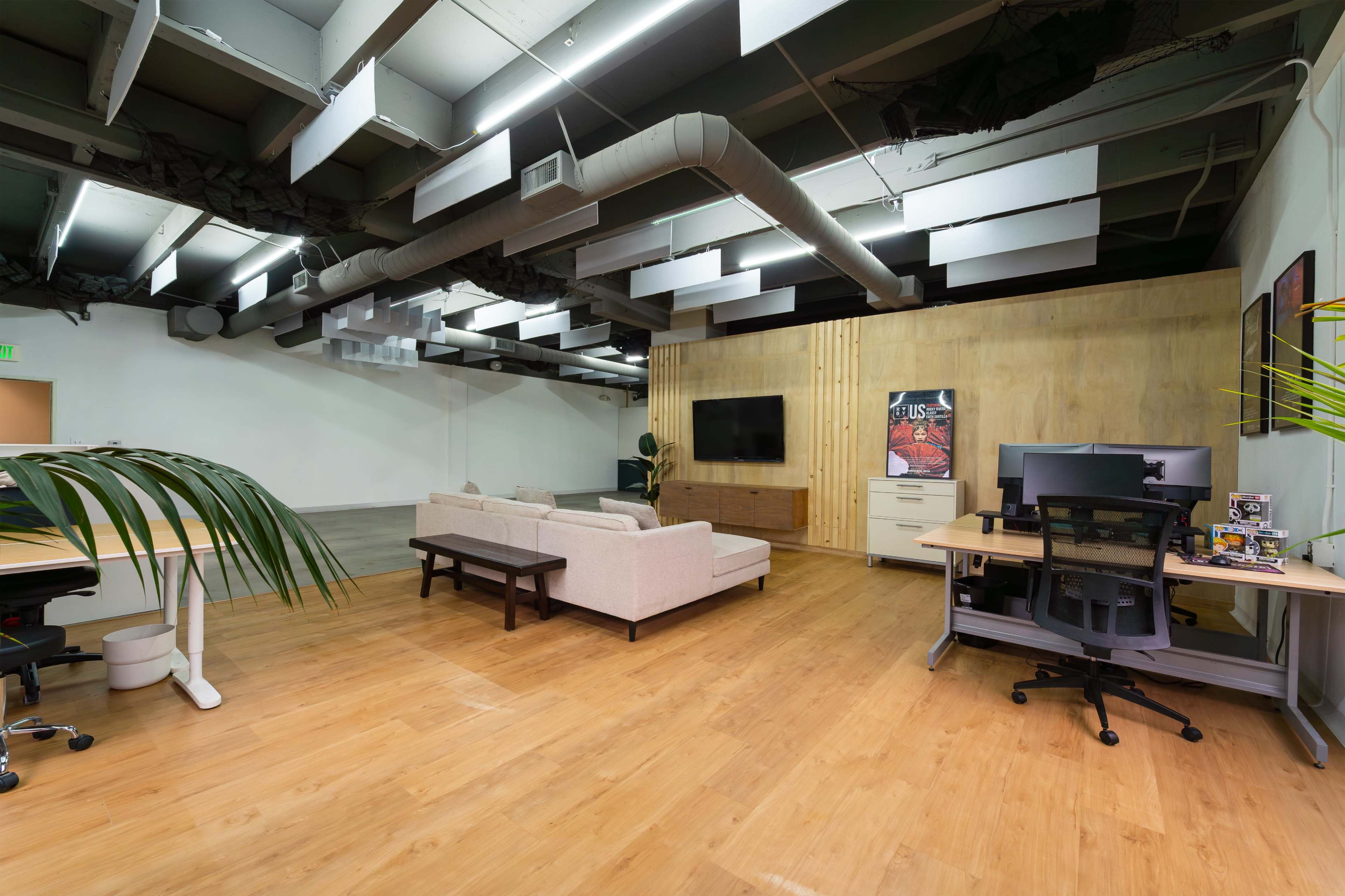 The image shows a spacious office interior with a couch, a desk with a computer, and a television mounted on a wooden wall.