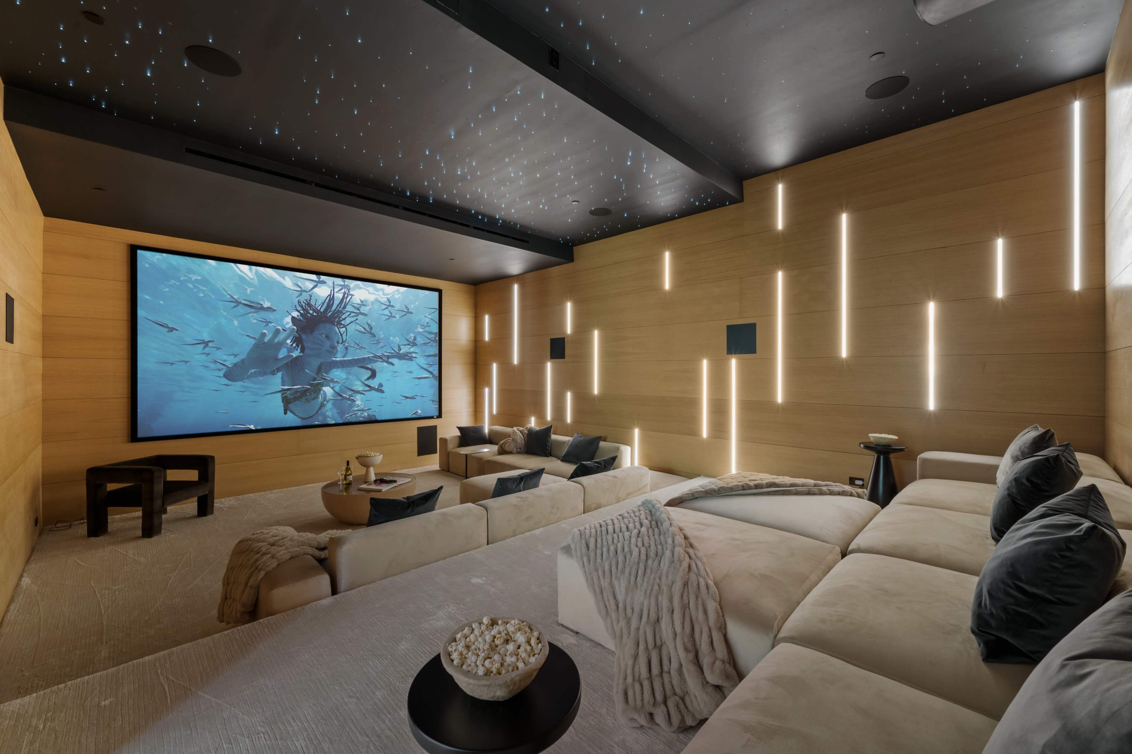 A modern home theater features a large screen displaying an underwater scene, surrounded by wooden walls and cozy seating.