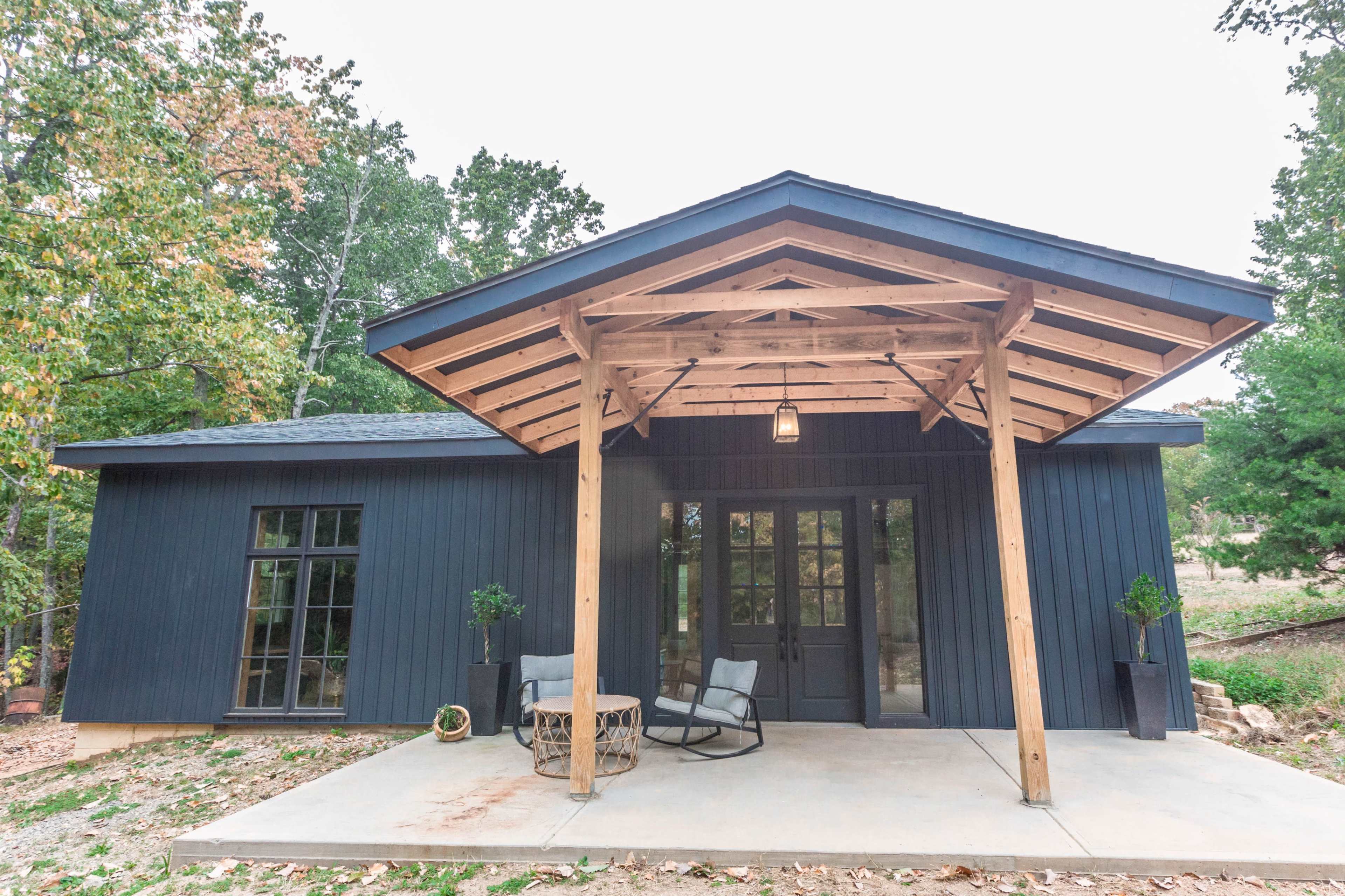 A modern house with a blue exterior and a wood-beamed porch, featuring two chairs and a small round table.