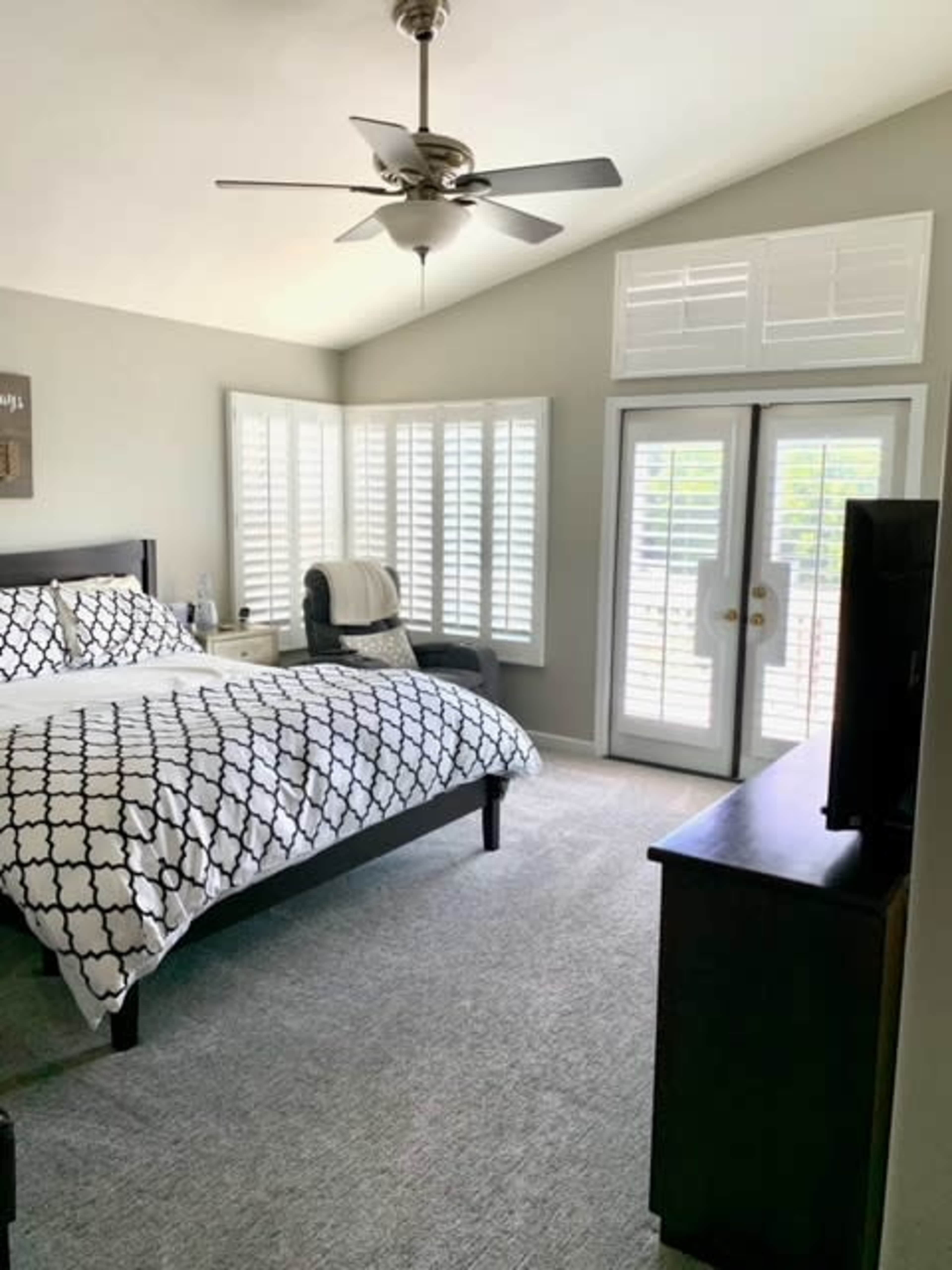 A spacious bedroom featuring a bed with a patterned duvet, a sitting area by large windows, and doors leading to an outdoor space.