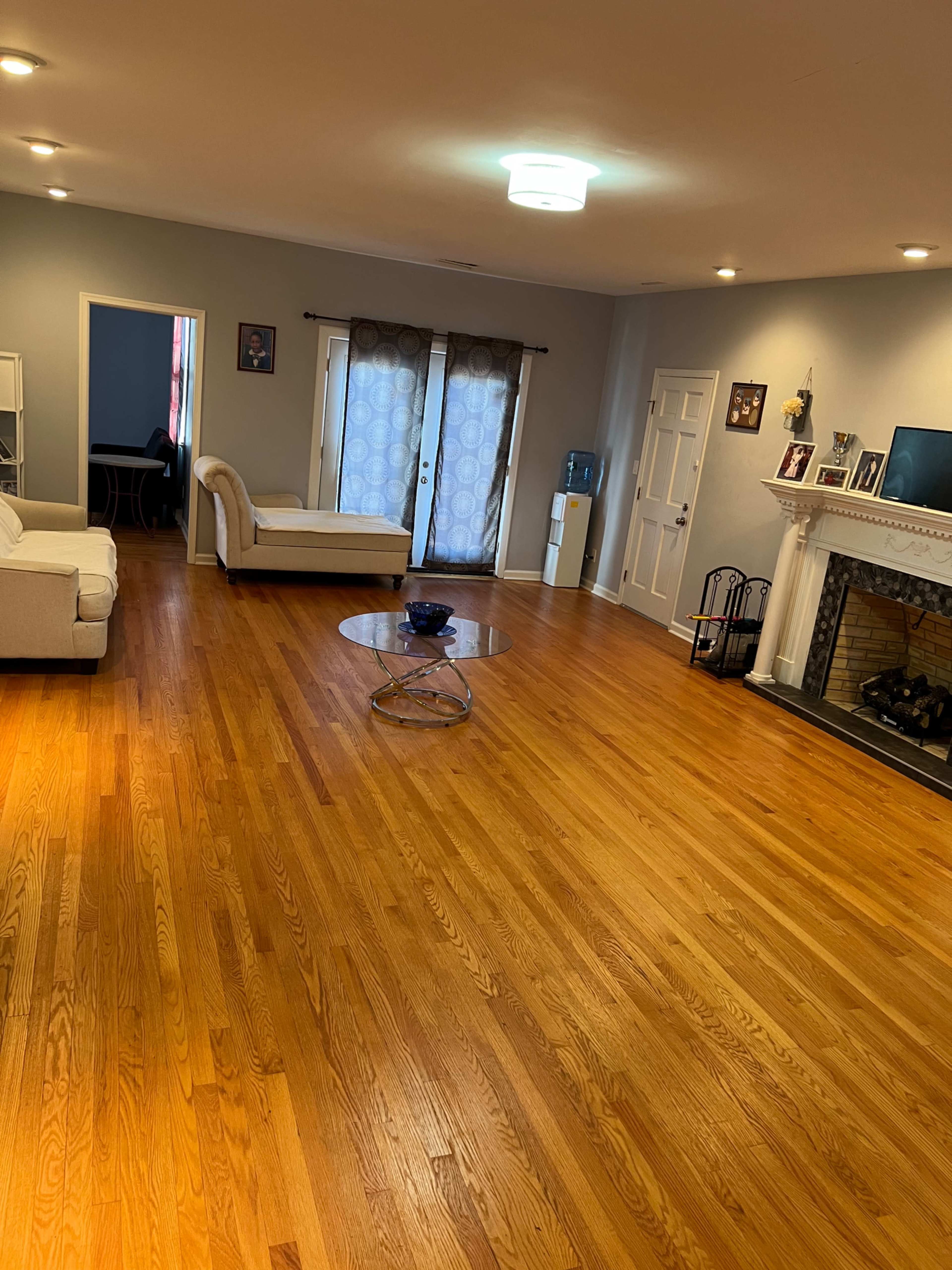 The image shows a spacious living room with hardwood floors, a coffee table in the center, and two sofas arranged around the area.