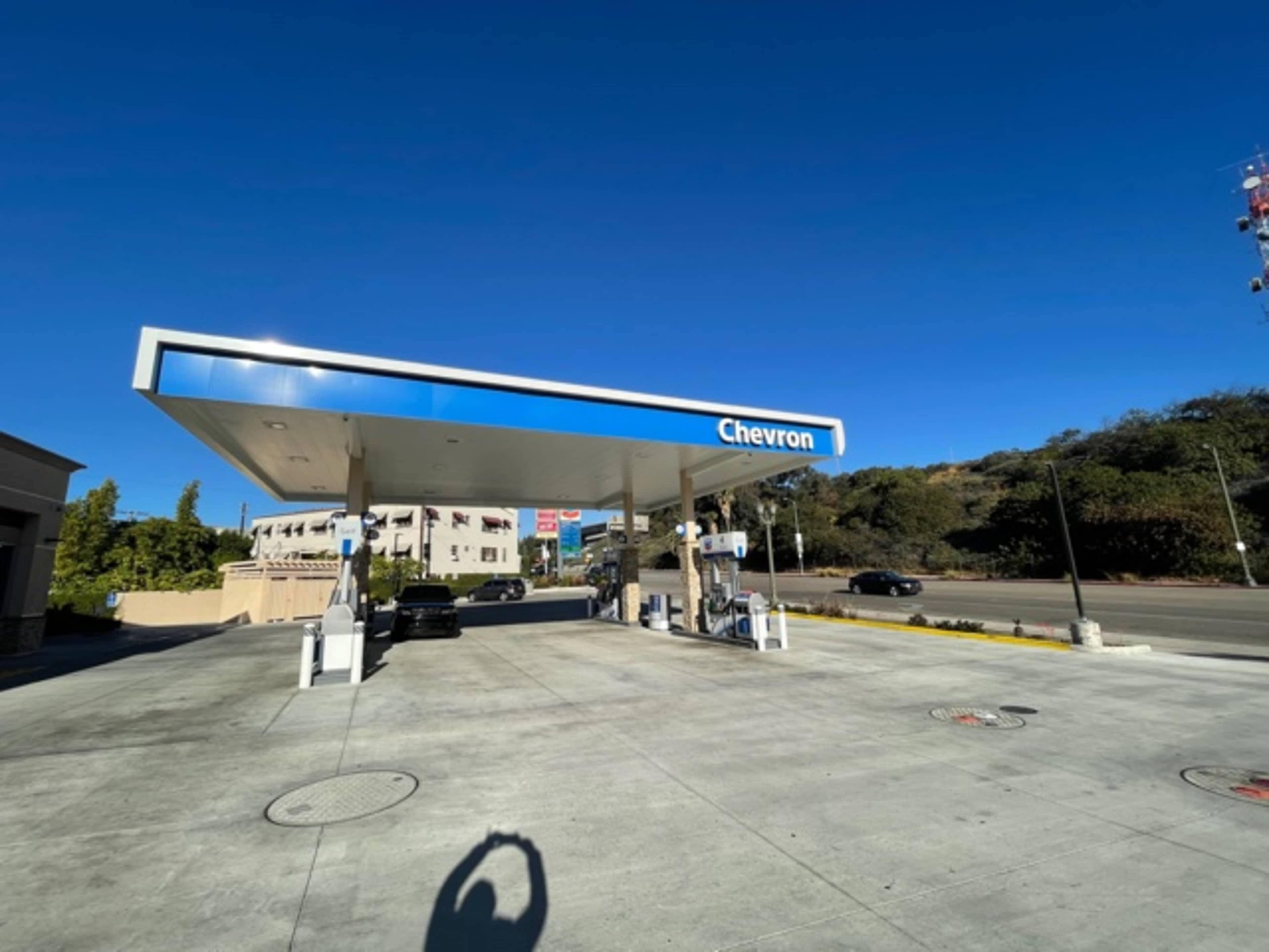 A Chevron gas station with a clear blue sky and hills in the background is shown.