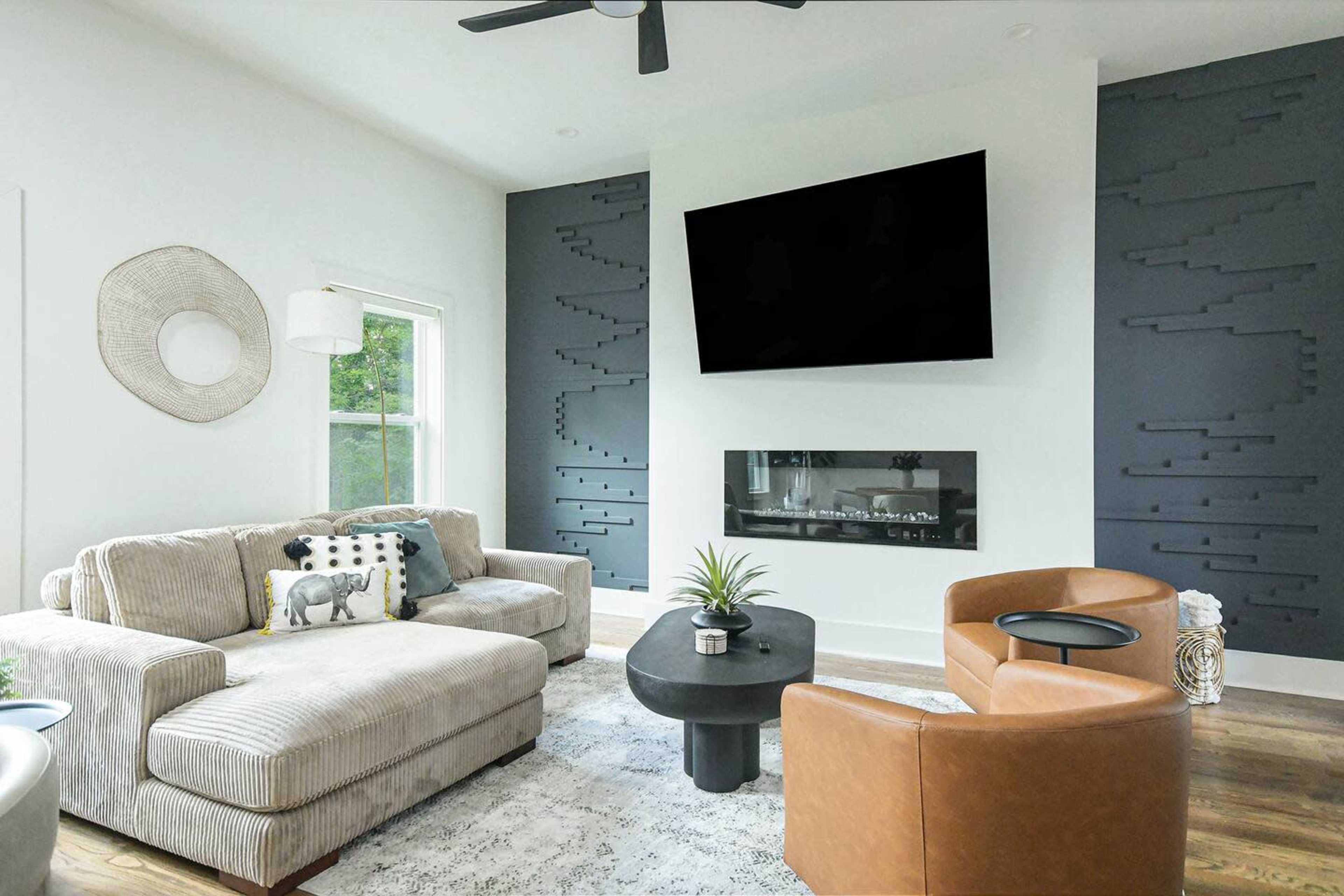 The living room features a sectional sofa, a coffee table, and a mounted television above an electric fireplace, with unique wall designs on either side.