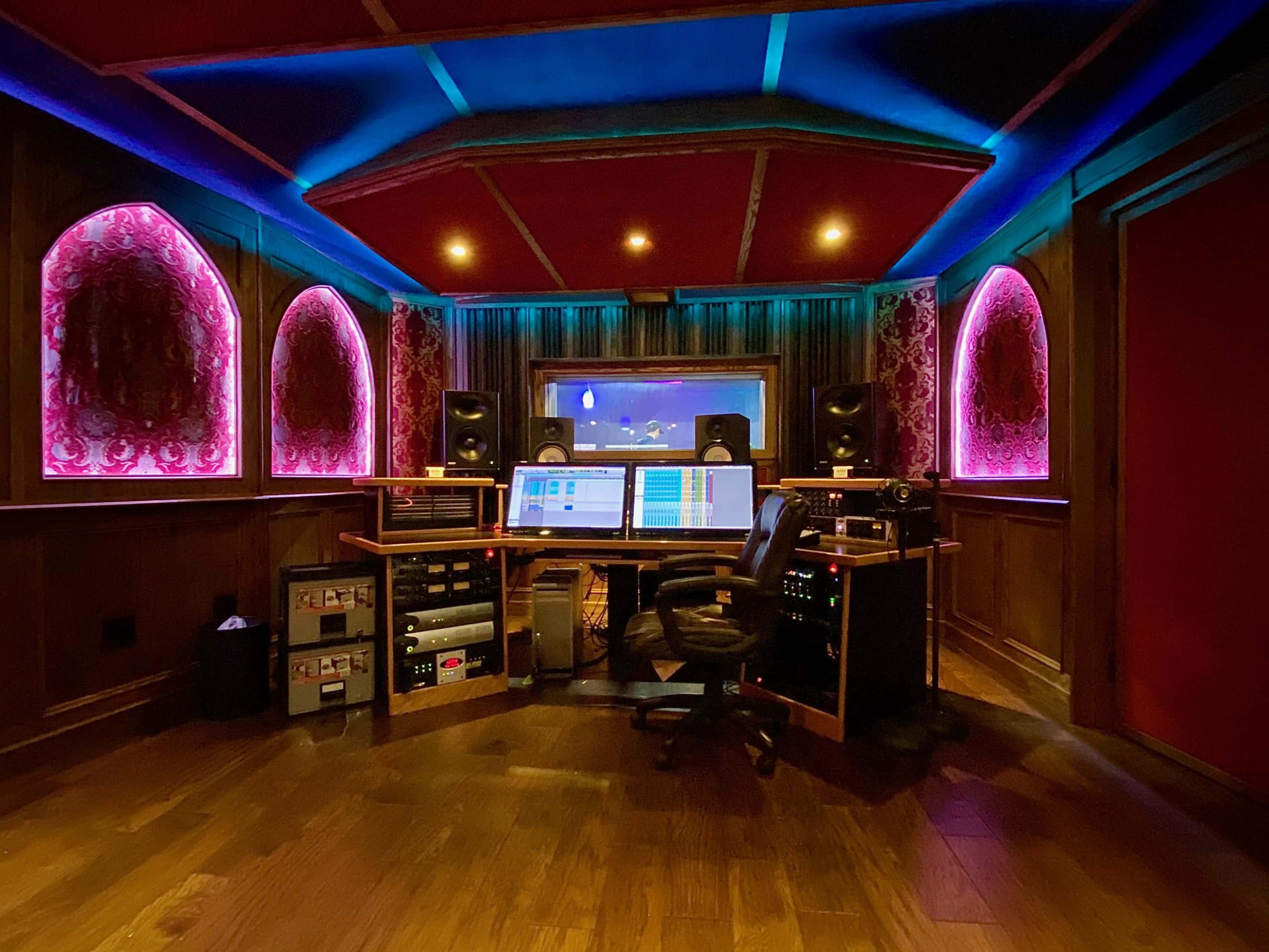 A modern recording studio with colorful lighting, a central mixer, and sound equipment arranged along wooden walls.