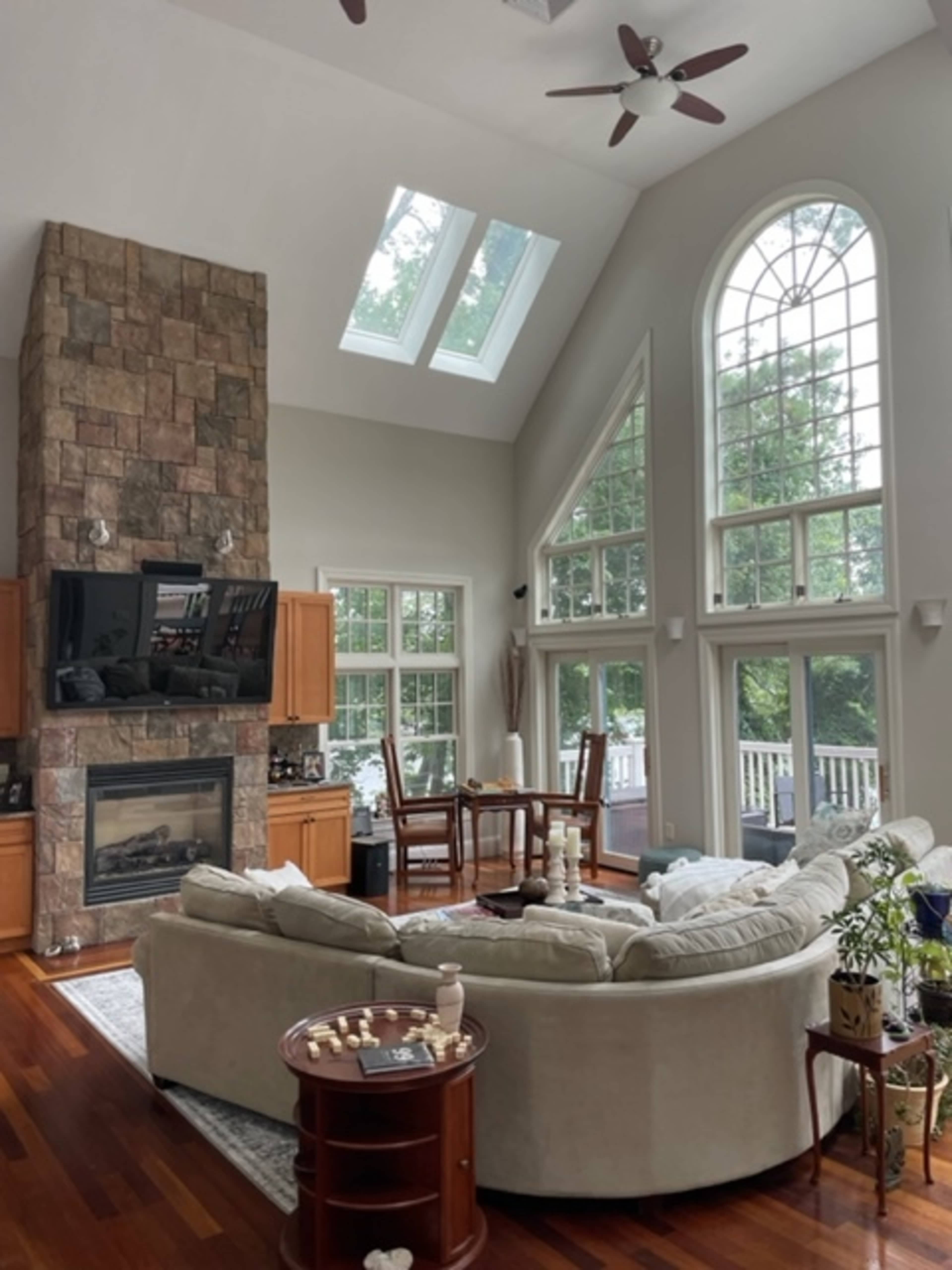 A spacious living room featuring a large stone fireplace, multiple windows allowing natural light, and a circular sectional sofa arranged around a coffee table.