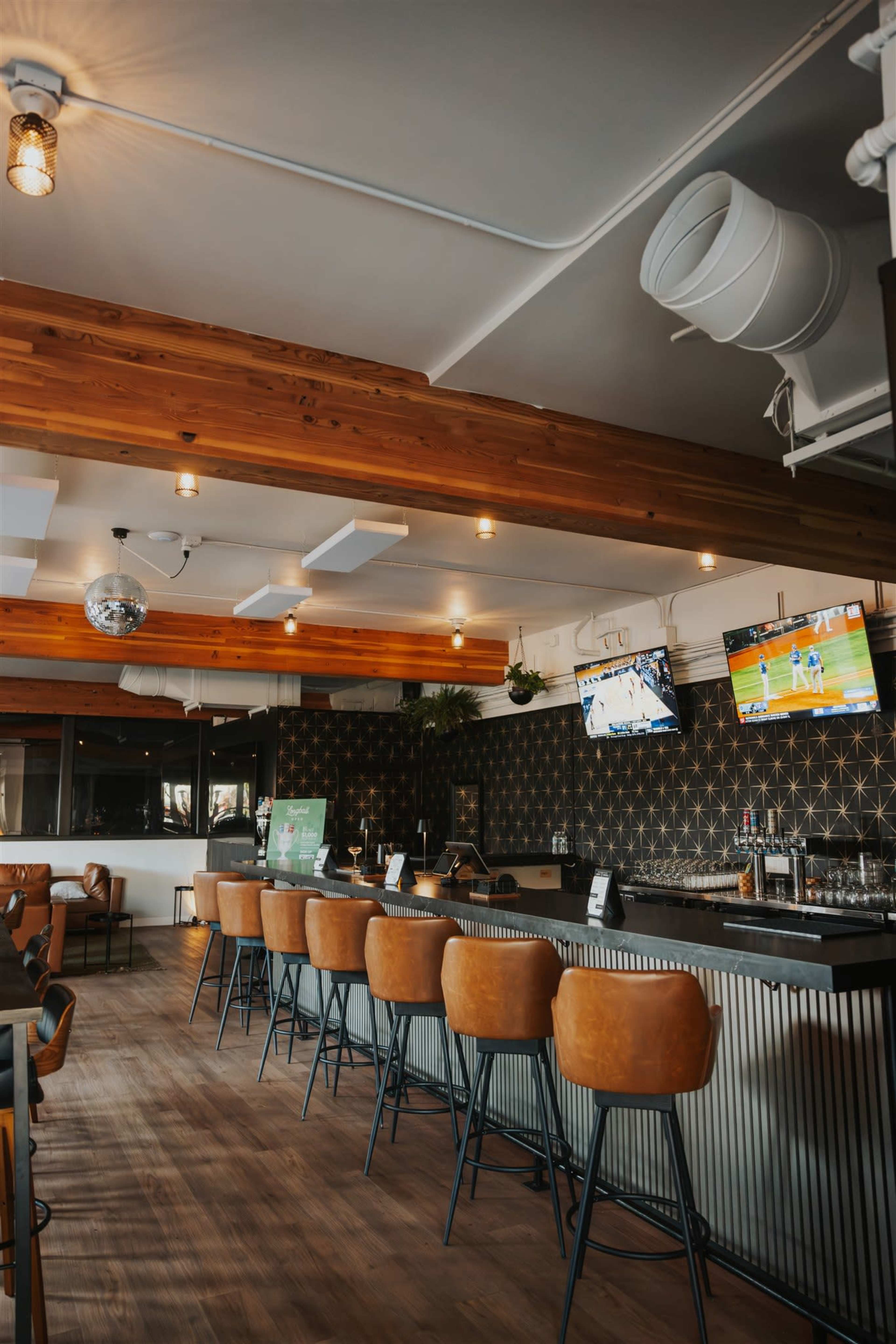 The image shows a modern bar interior with a long counter, several high stools, and multiple TVs displaying sports.