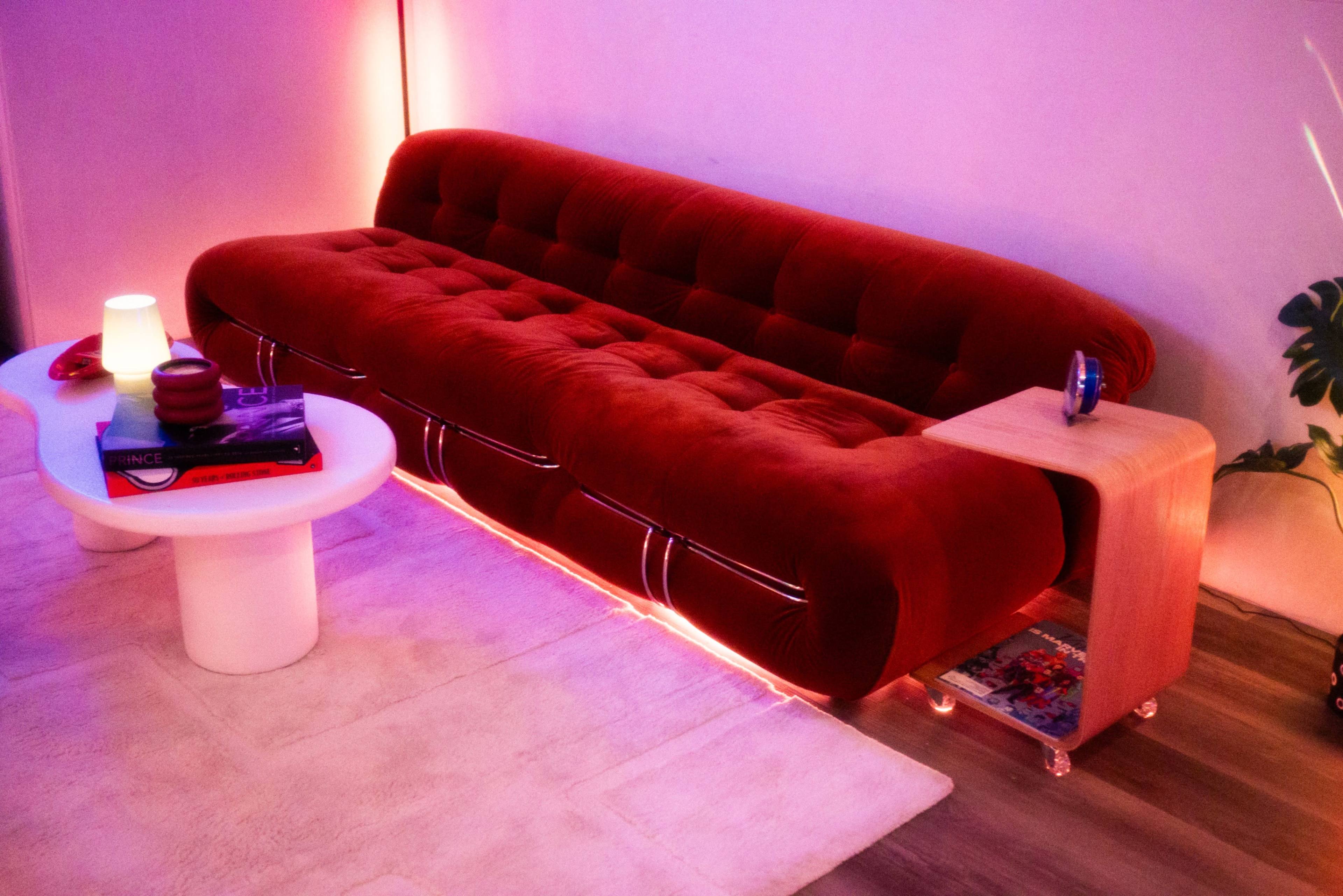 A red velvet sofa with tufted upholstery sits next to a white coffee table in a softly lit room.