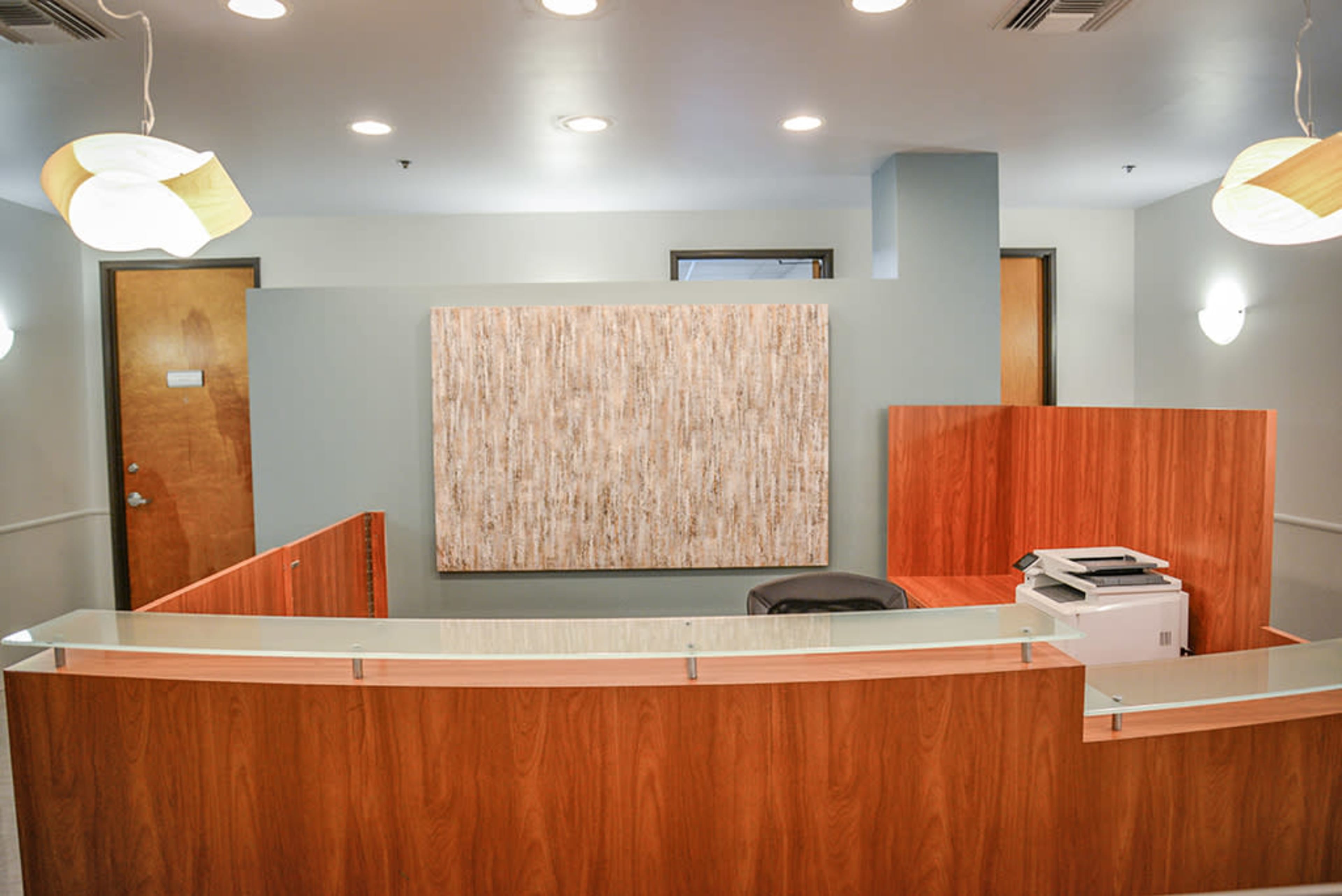 A reception area features a wooden front desk, a printer, and a large abstract wall art piece.
