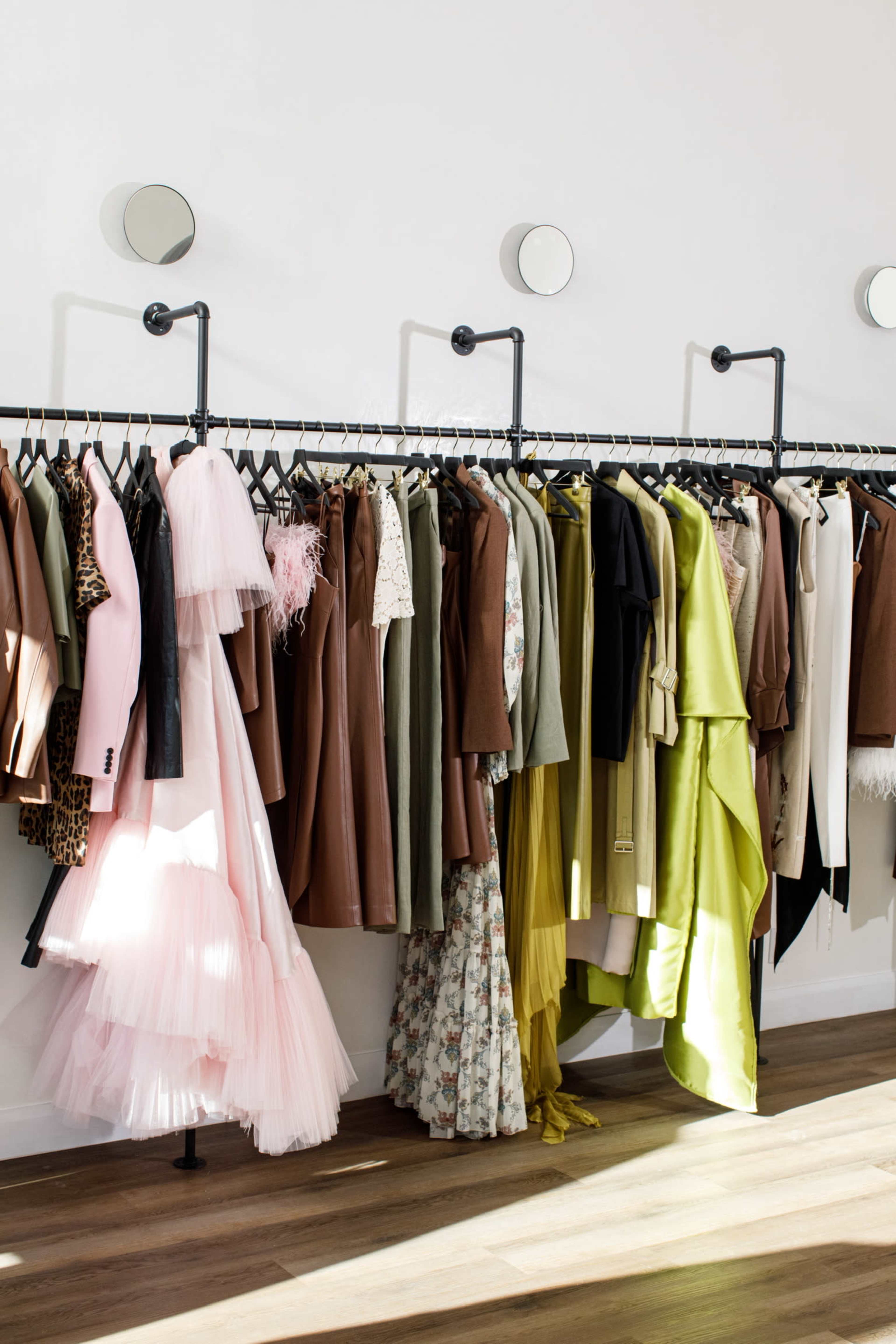 The image shows a clothing rack displaying a variety of garments, including dresses, blazers, and tops in muted and vibrant colors, arranged neatly along the wall of a retail space.