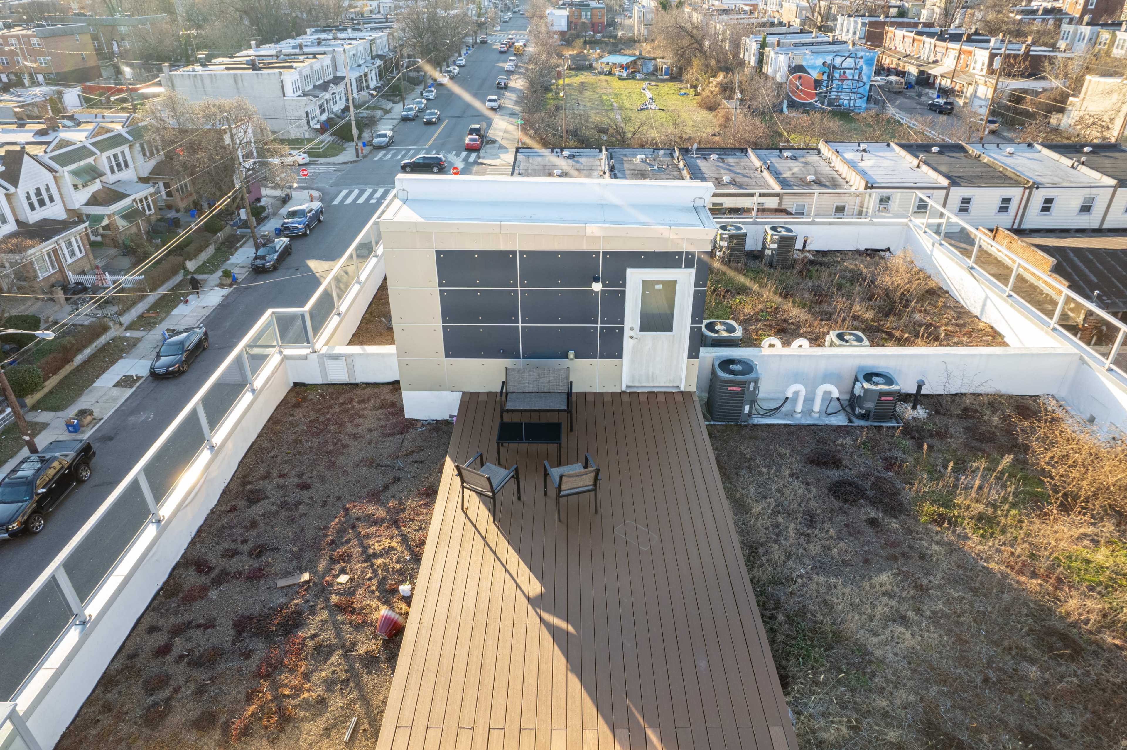 A rooftop terrace with a wooden deck, featuring a small table and chairs, overlooking a residential neighborhood and open space.