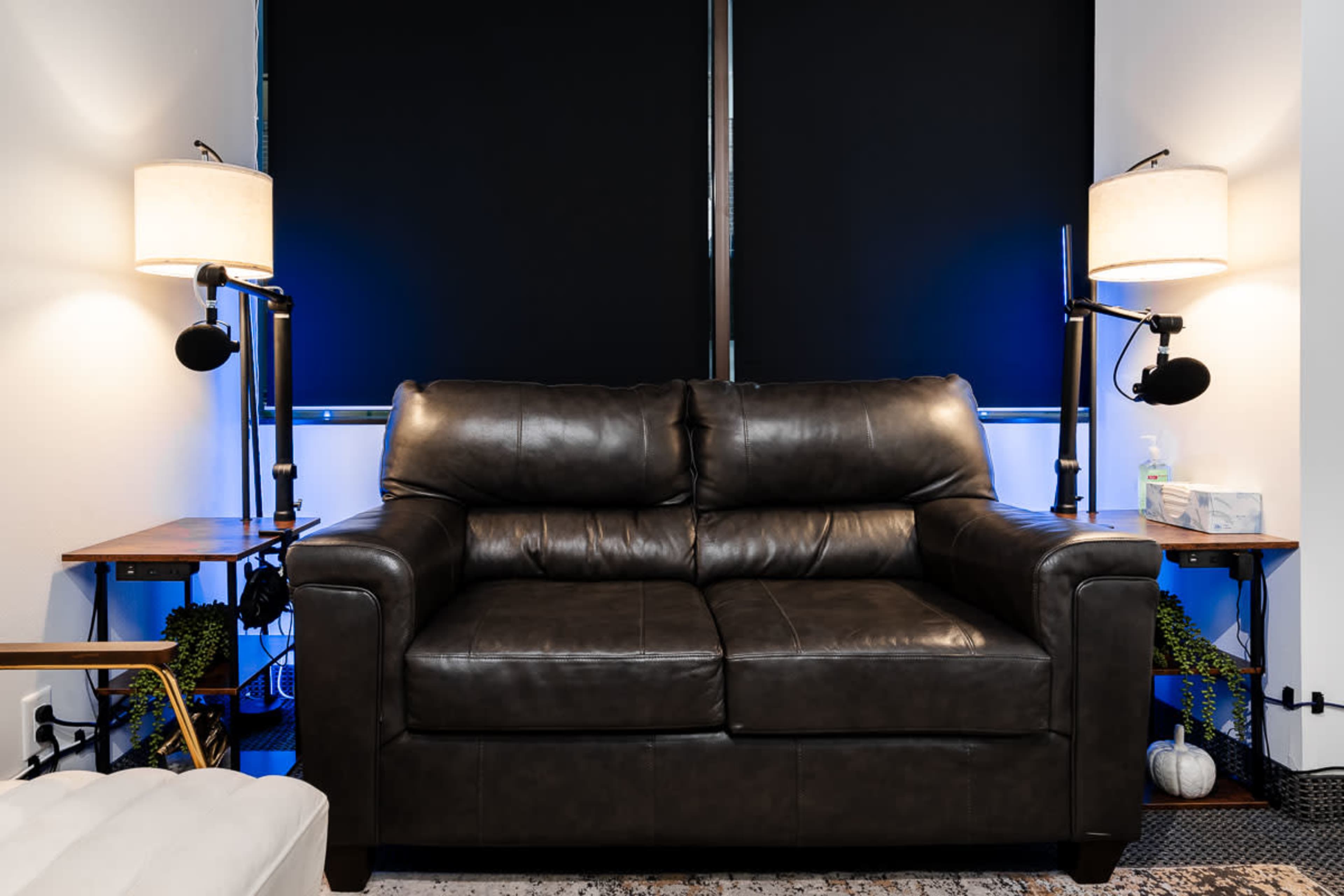 A brown leather sofa is positioned between two lamps on side tables, with dark window coverings in the background.