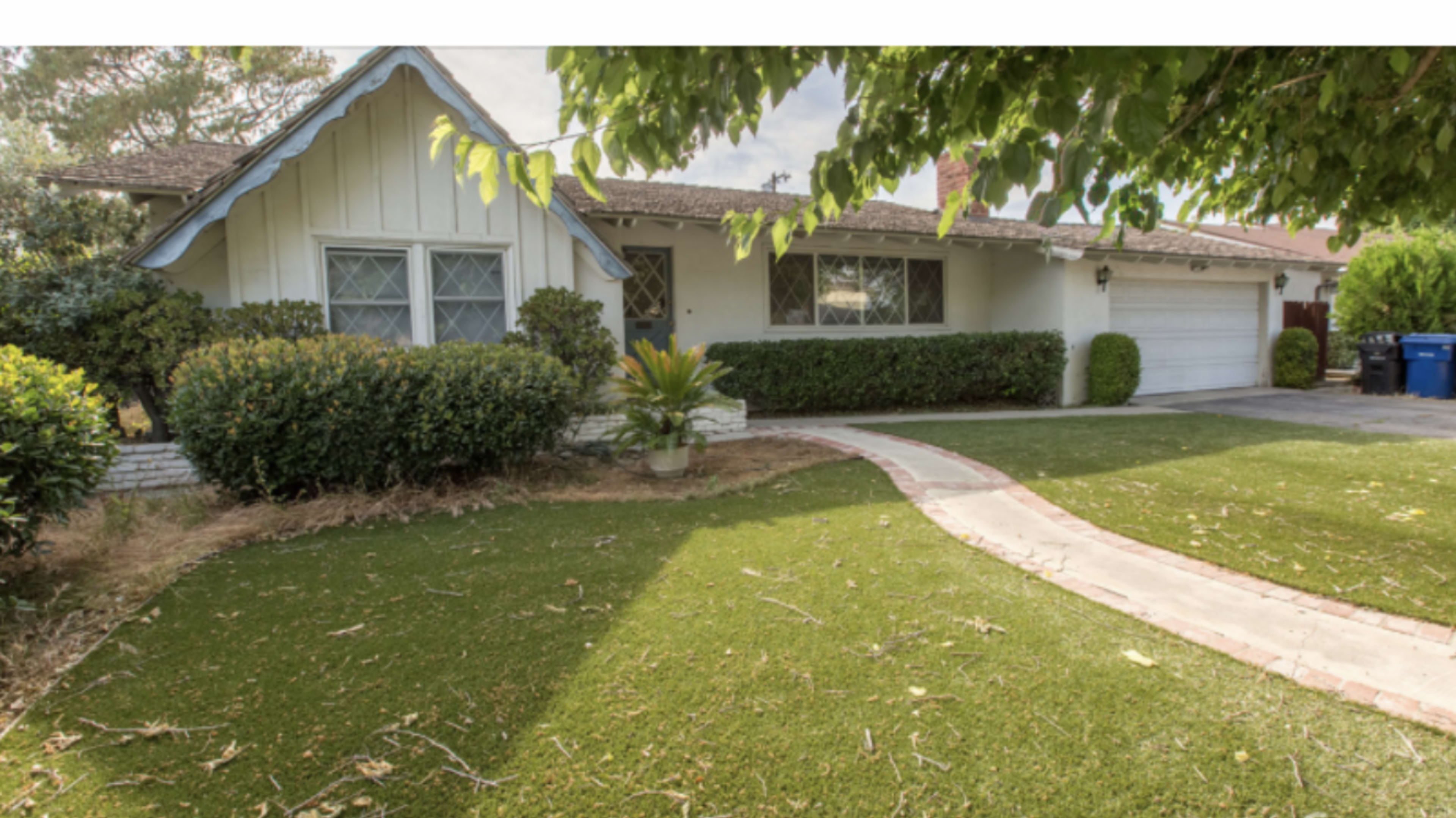 A residential house with a white exterior, blue trim, a well-maintained lawn, and a curved pathway leading to the front door.