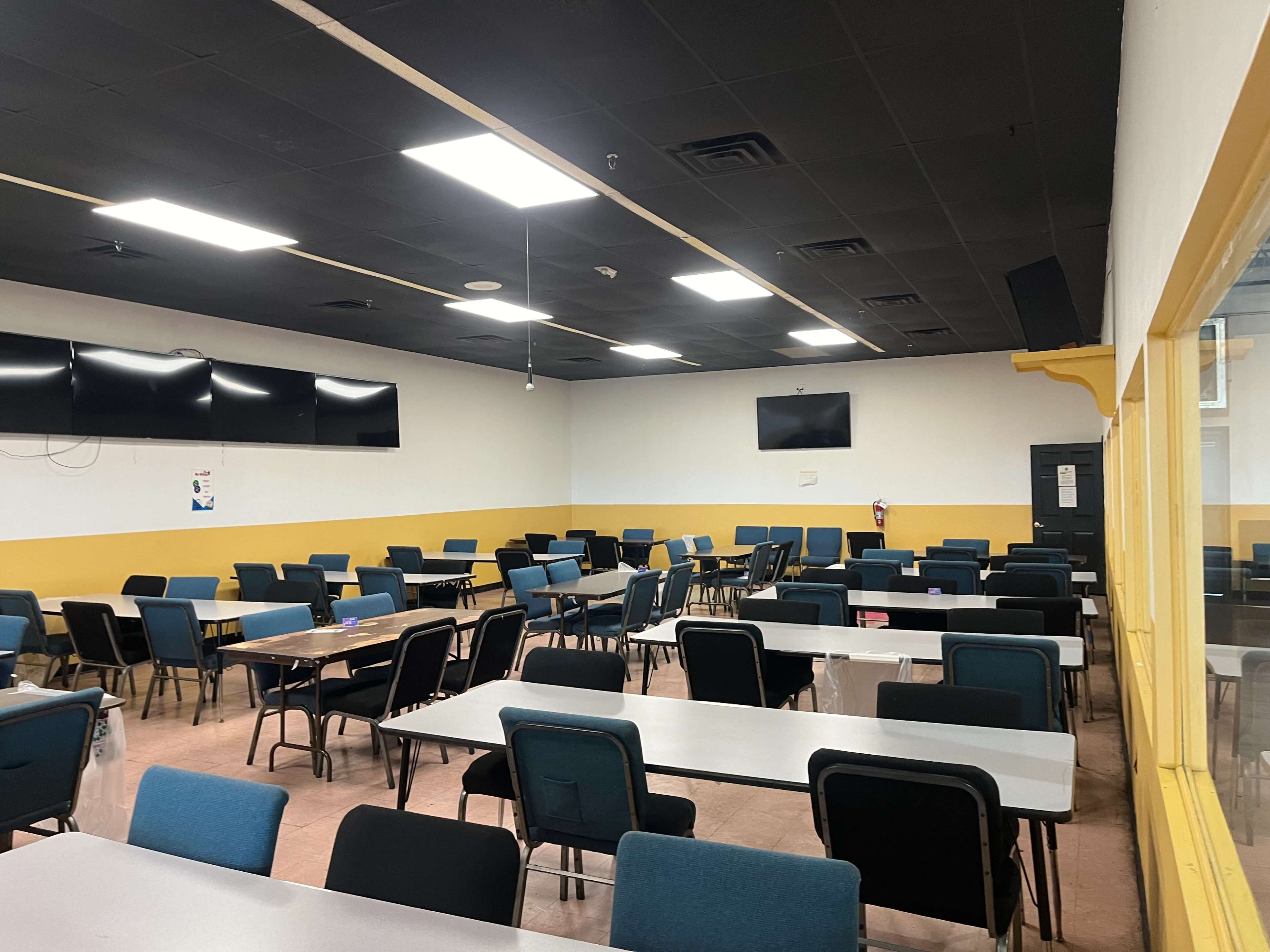A spacious dining area with rows of tables and chairs, and several wall-mounted televisions.