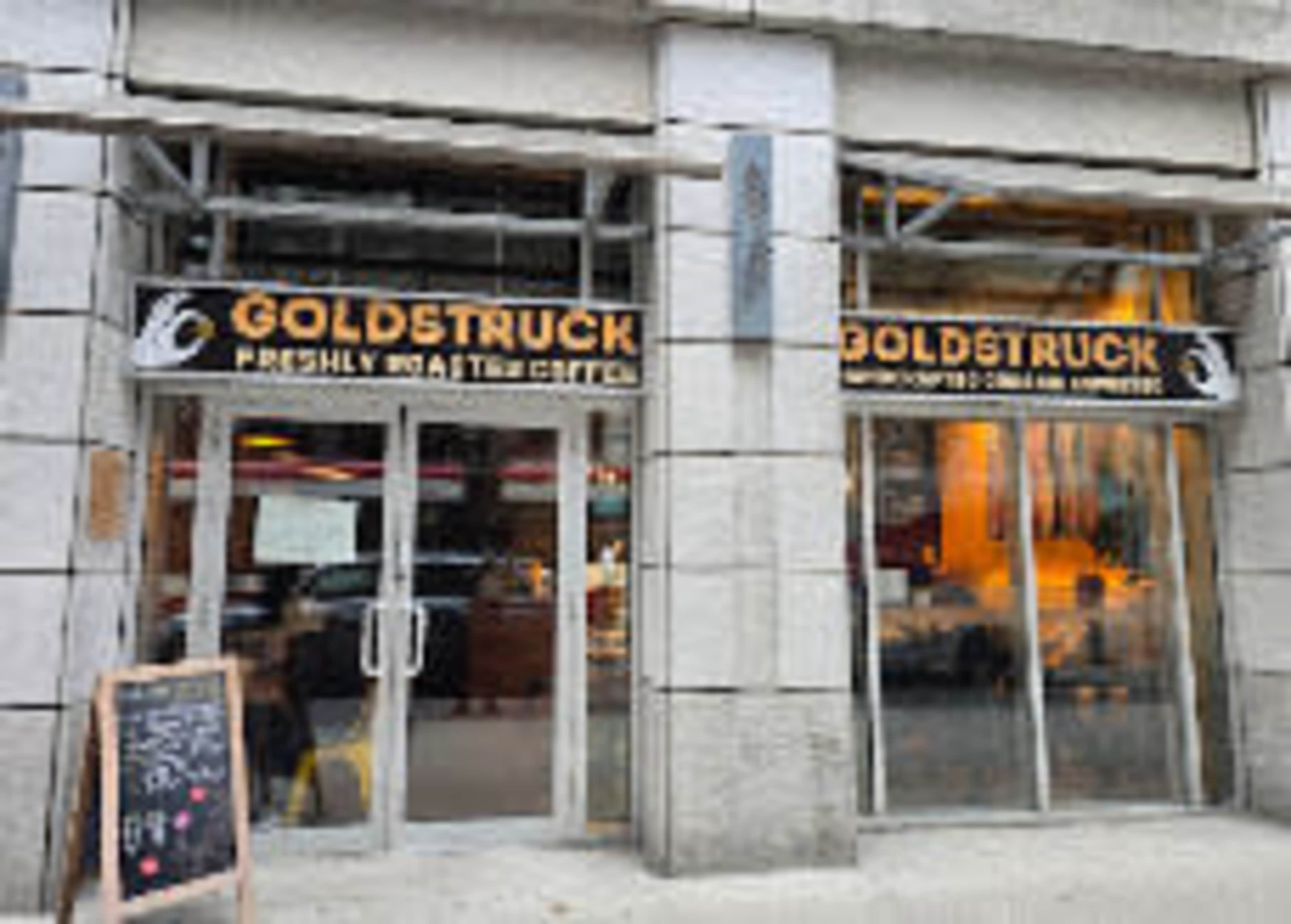 The image shows the entrance of a coffee shop named "Goldstruck" with large windows and a sign indicating freshly roasted coffee.